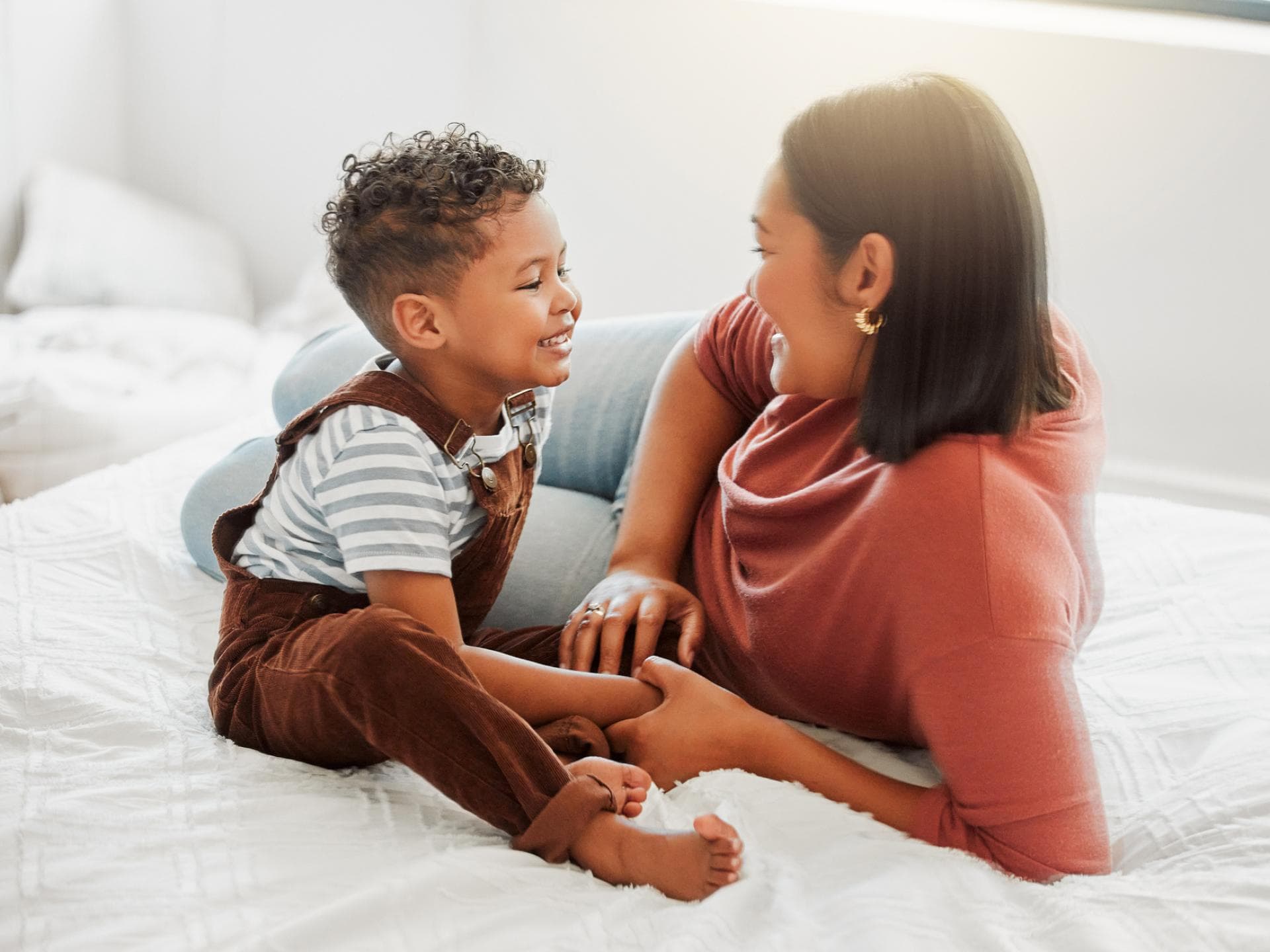 Kindern Grenzen setzen ist für Eltern oft nicht ganz leicht. Mutter und Sohn liegen auf dem Bett und unterhalten sich.