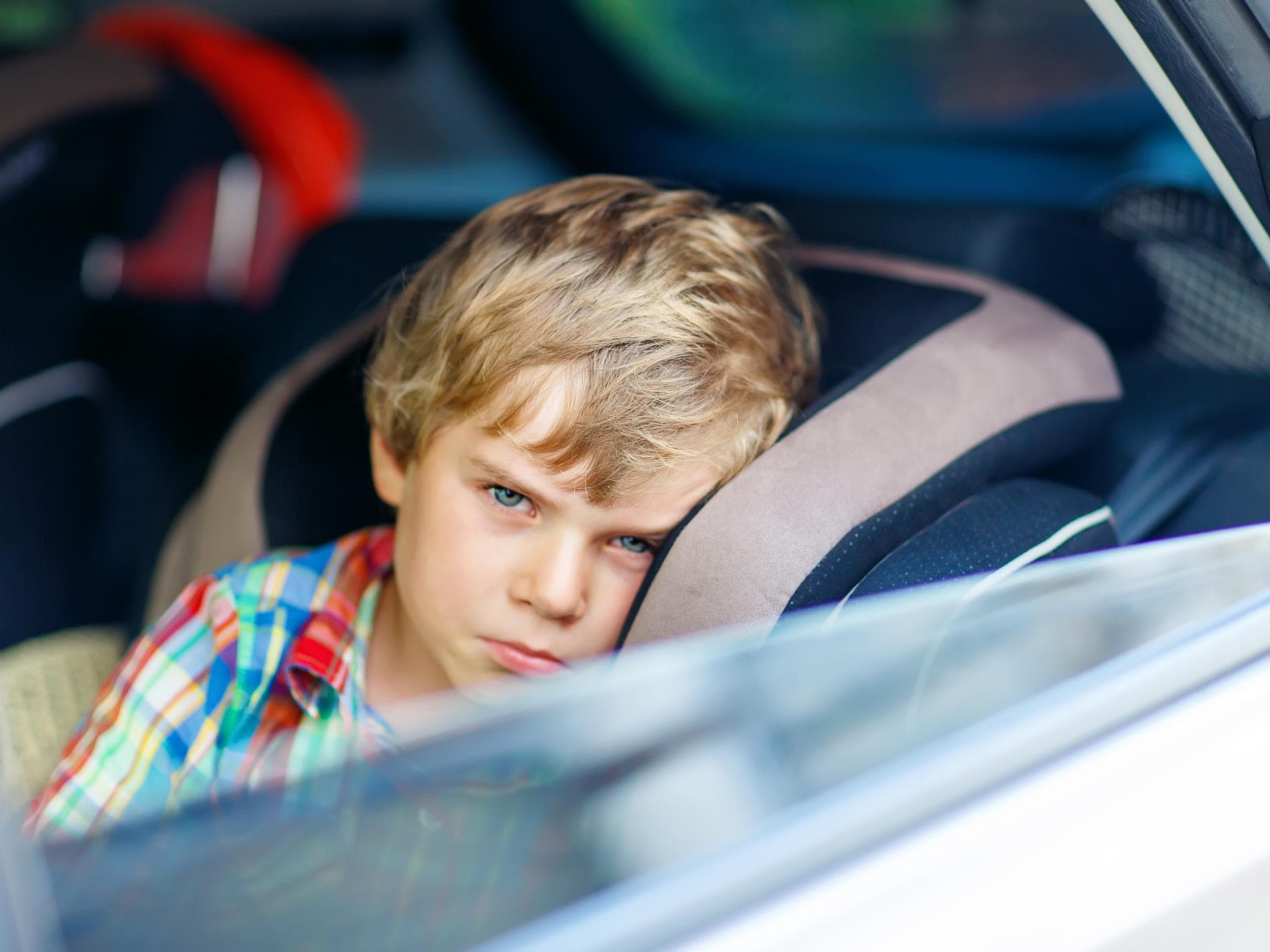 Darf man sein Kind alleine im Auto lassen? Dieses Frage stellen sich viele Eltern früher oder später. Ein kleiner Junge schaut aus dem offenen Autofenster.