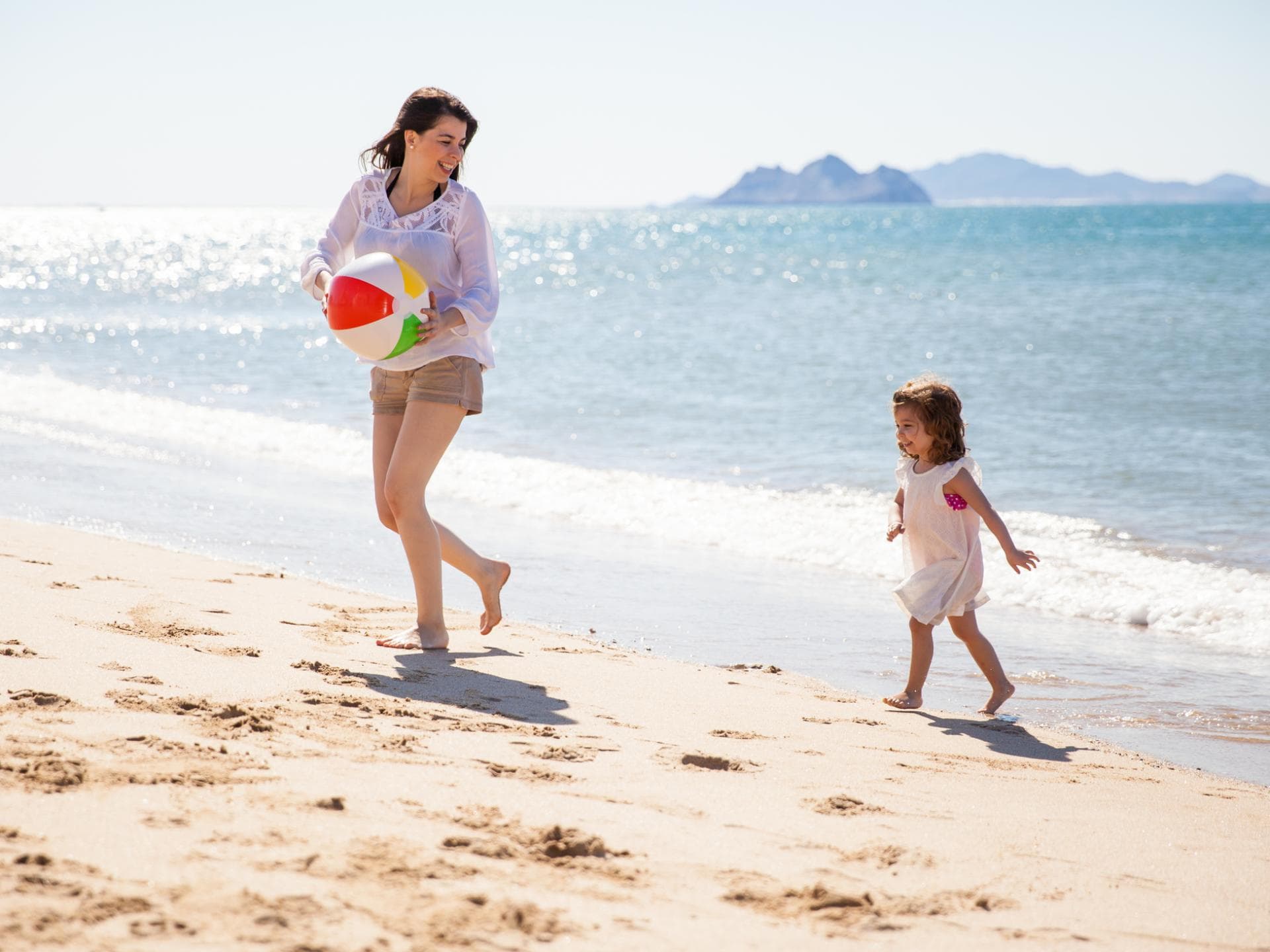 Eine Reise-Nanny kann die Eltern unterstützen. Junge Frau spielt mit Kind am Strand.