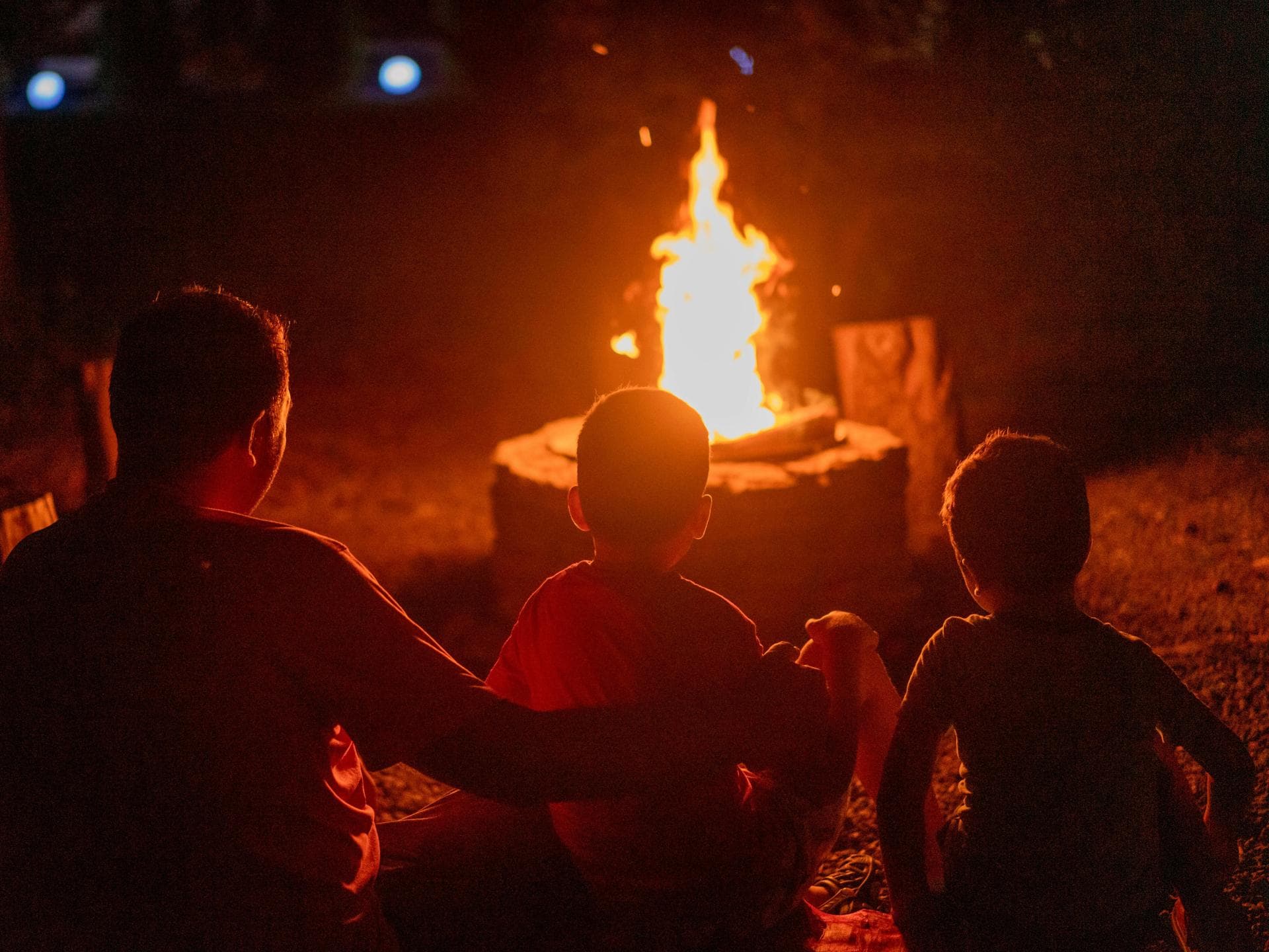 Ein Vater sitzt mit seinen beiden Kindern am Lagerfeuer. 