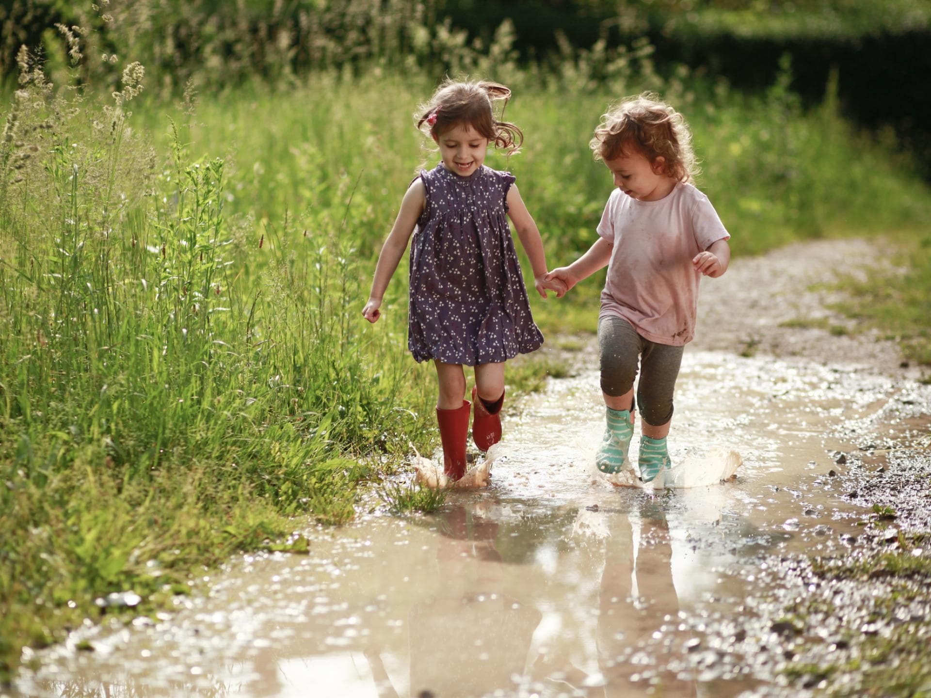 Kinder lieben die Natur – und Eltern können diese Begeisterung unterstützen. Zwei Kinder laufen durch eine Pfütze.