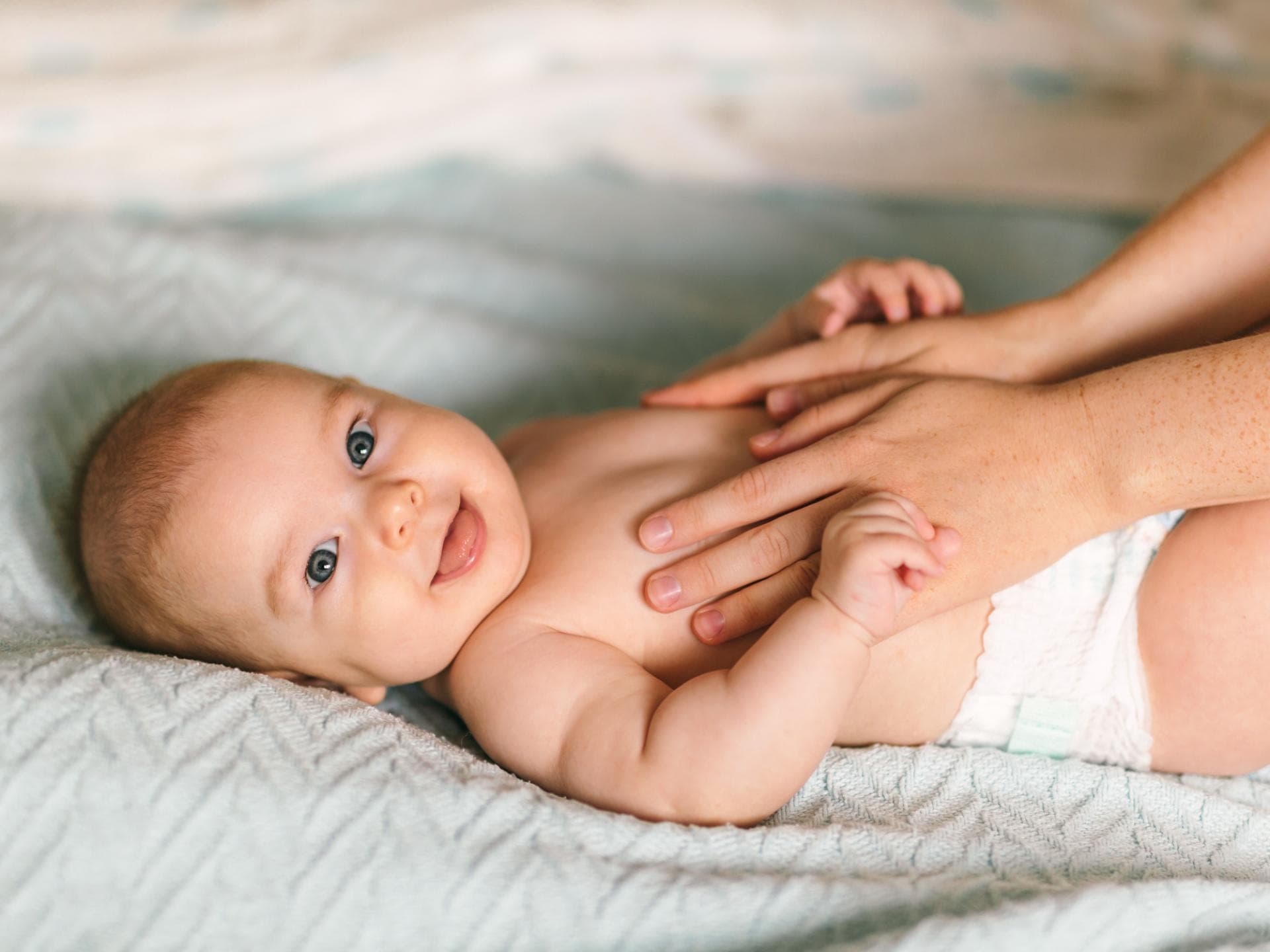 Bei der Säuglingspflege gibt es für Eltern einiges zu beachten. Baby liegt lächelnd auf einer Decke.