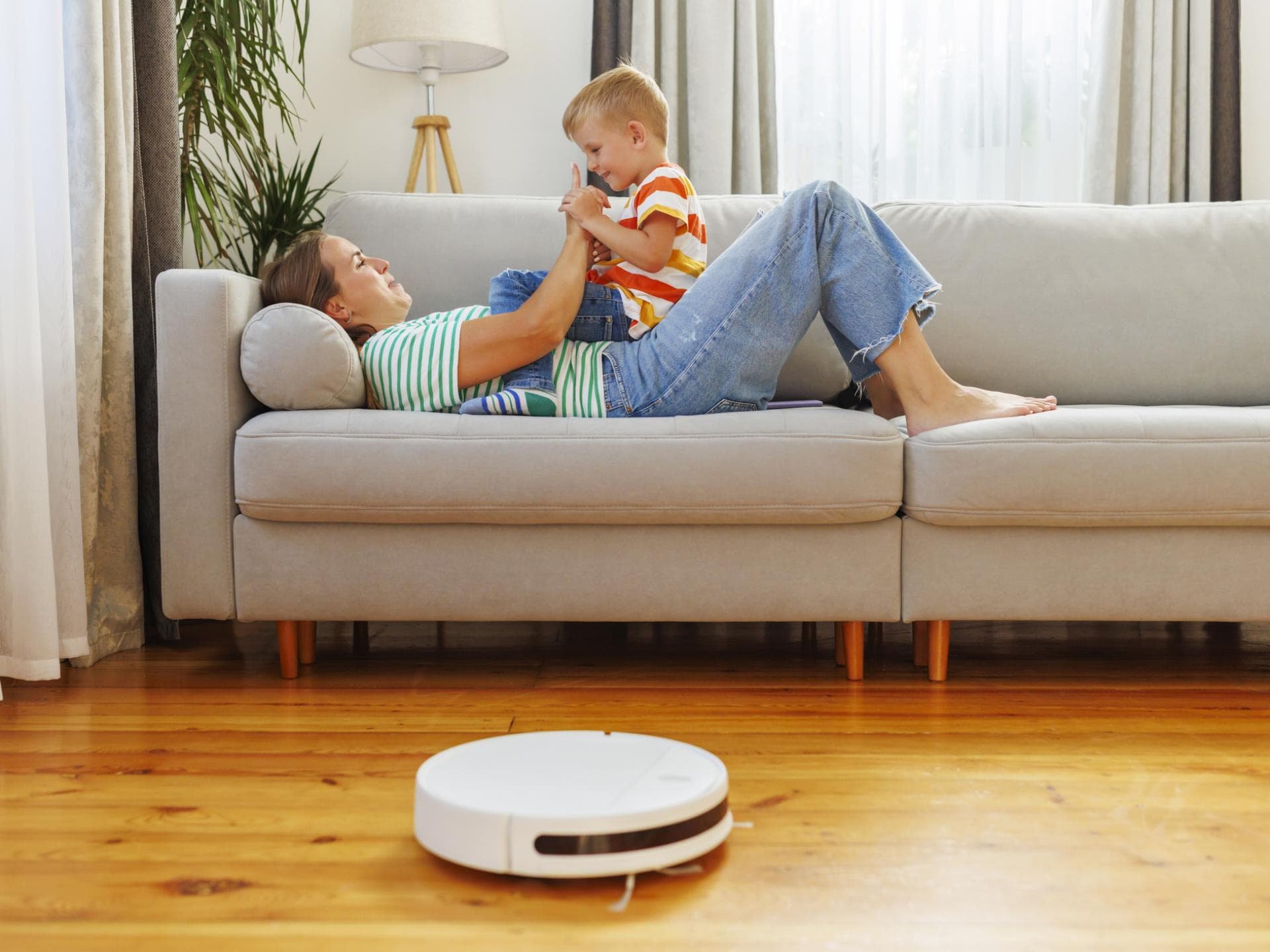 Mutter und Kind sitzen auf dem Sofa vor einem Saug-Roboter.