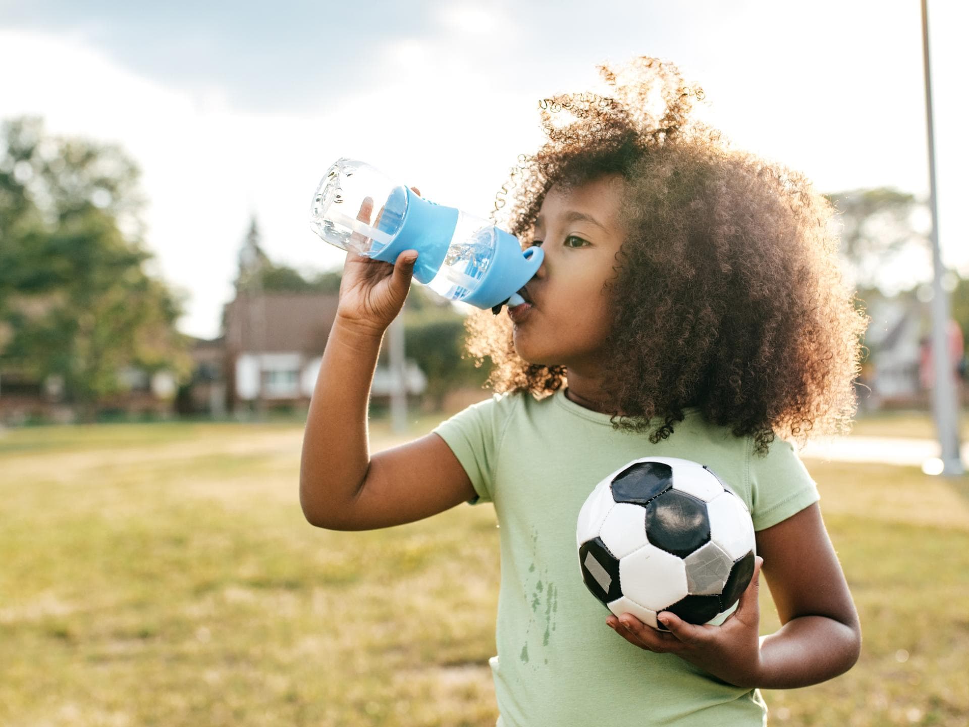 Kind mit Mini-Fußball trinkt aus einer Trinkflasche.