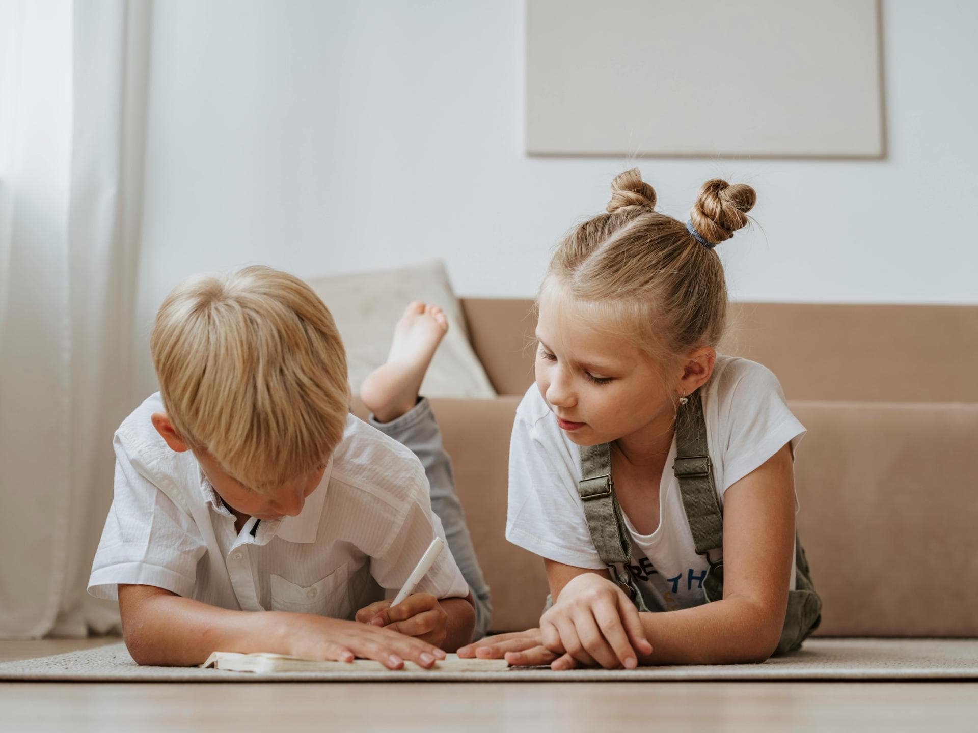 Zwei Kinder üben zusammen schreiben auf dem Wohnzimmerboden. 