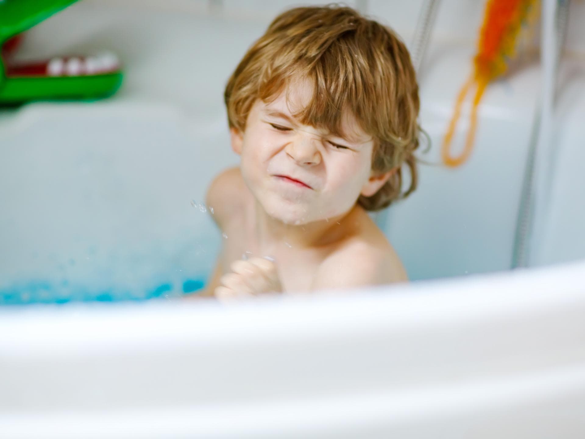 Euer Kind will nicht baden? Das kommt häufig vor. Ein kleiner Junge sitzt in der Badewanne und kneift die Augen zusammen.