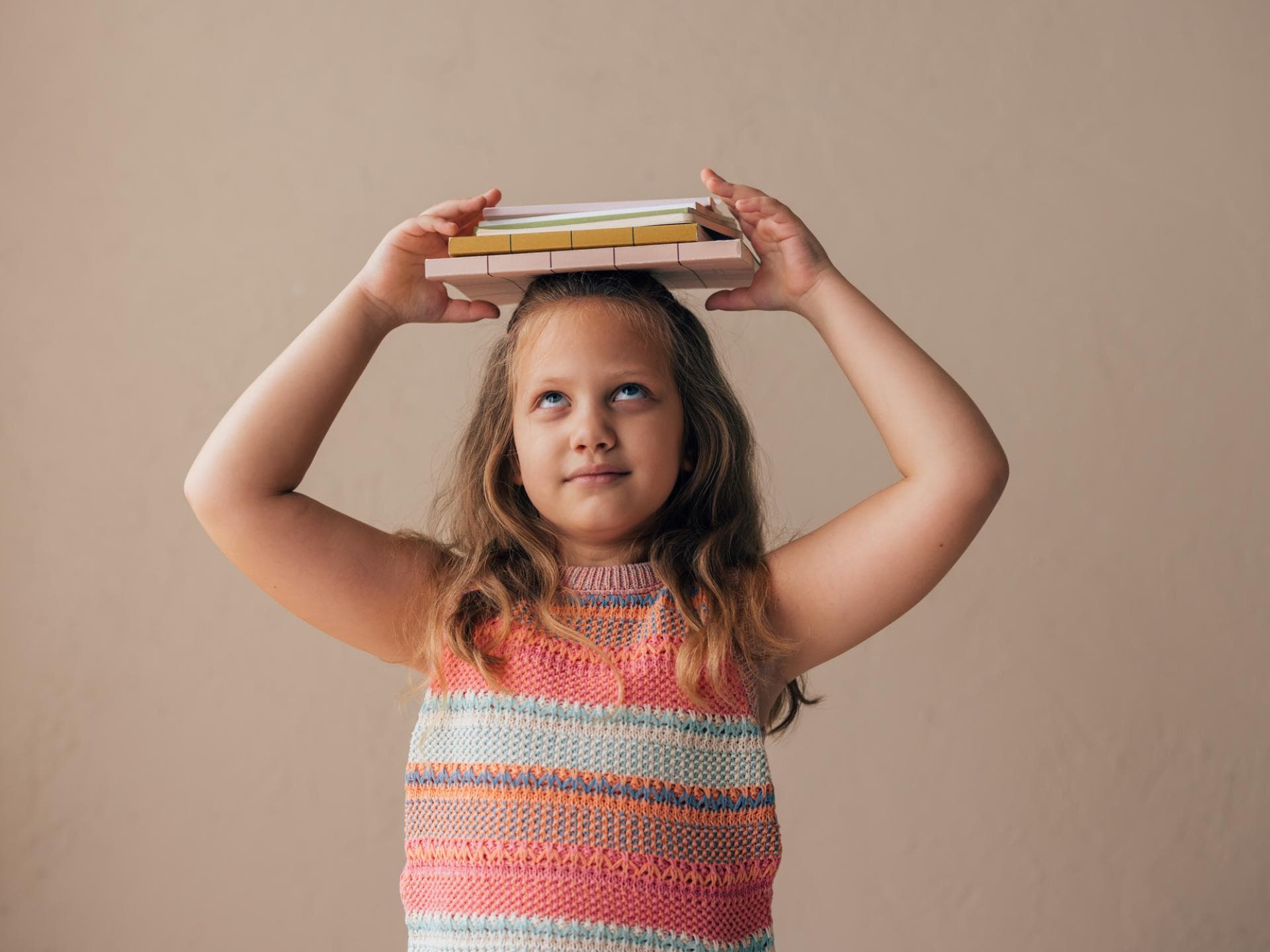 Mädchen balanciert Bücher auf dem Kopf.
