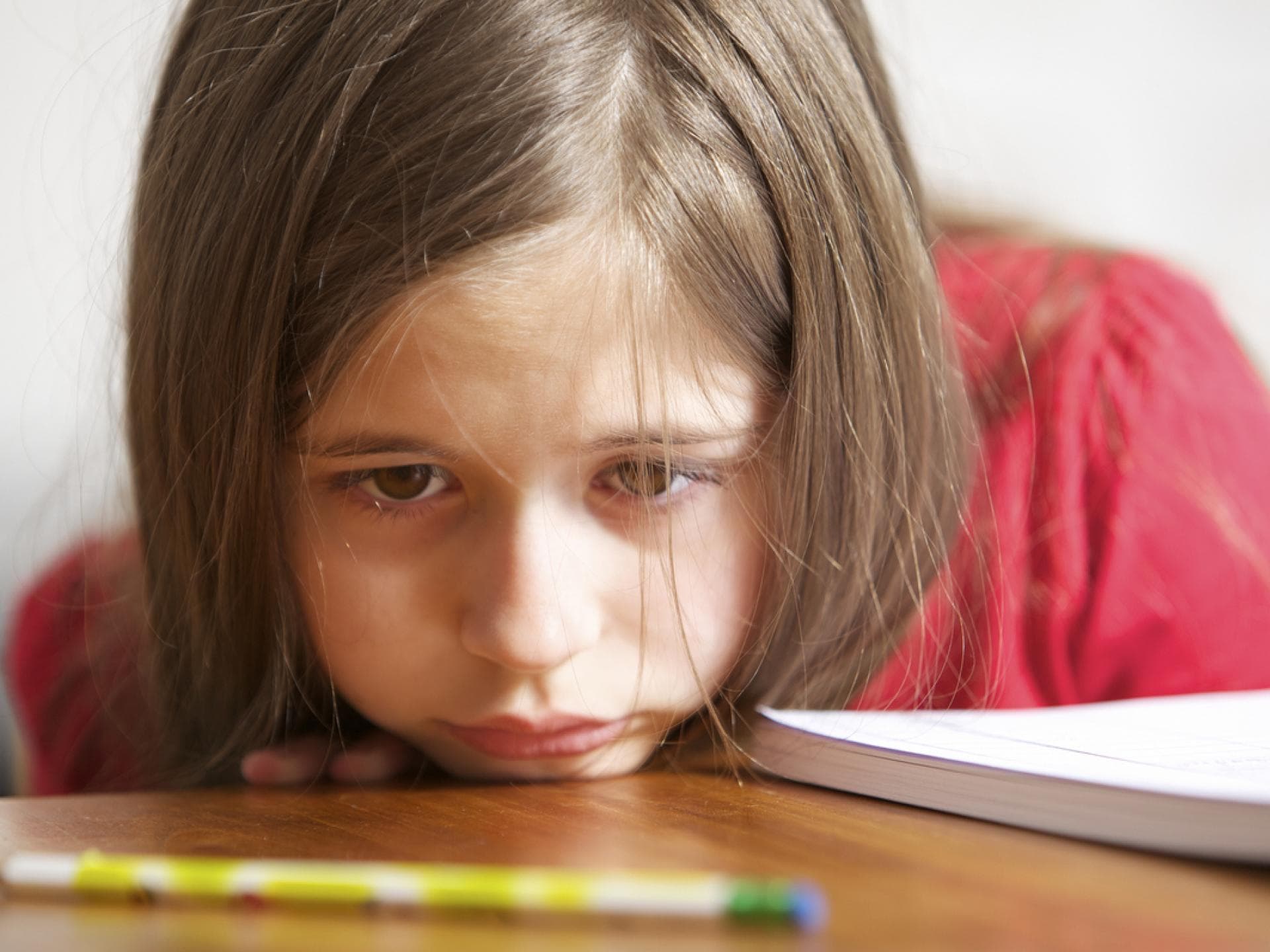Permanenter Leistungsdruck führt zum Gehetzes-Kind-Syndrom. Trauriges Mädchen legt den Kopf auf den Schreibtisch.