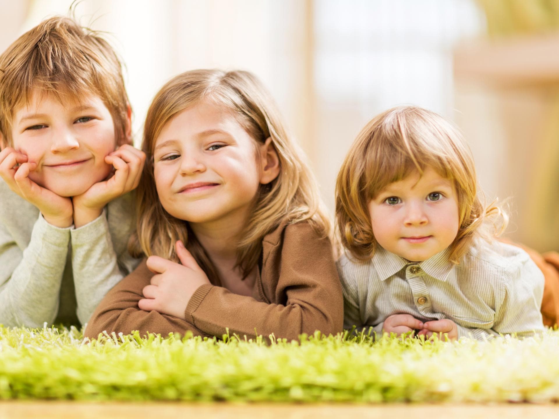 Drei Kinder liegen auf dem Teppich.
