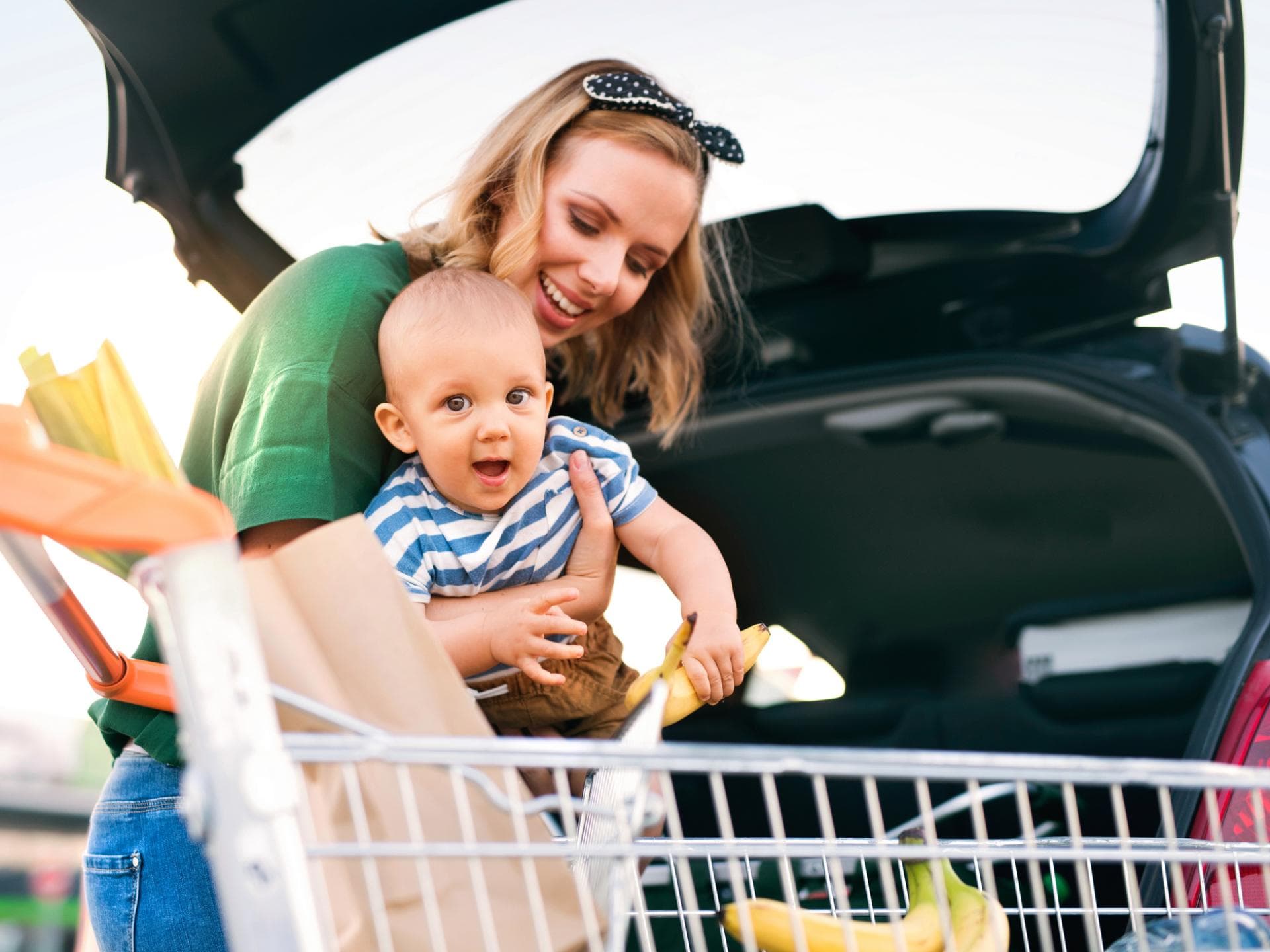 Mutter mit Baby und Einkaufswagen am Auto