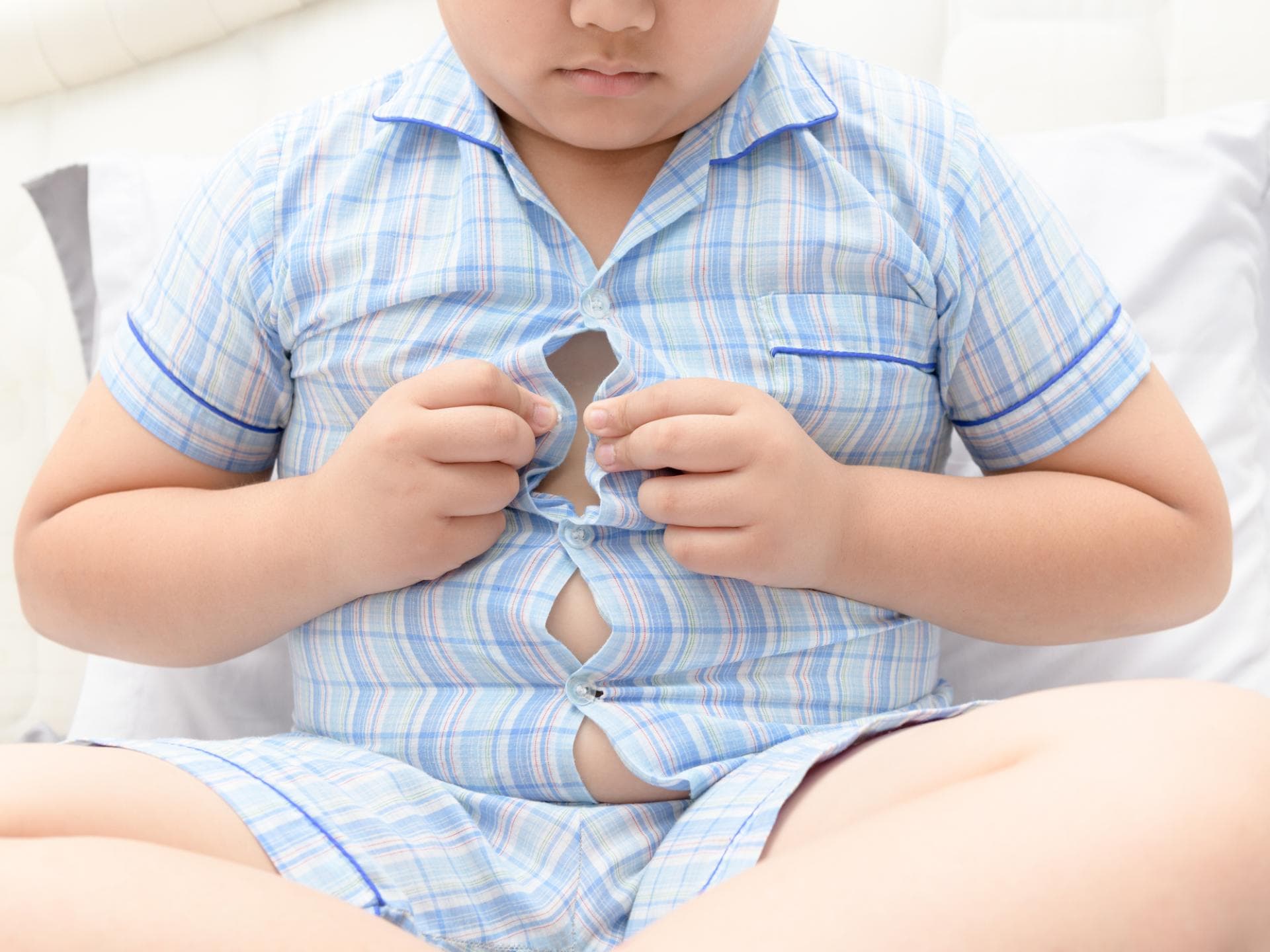 Manchmal ist es überraschend, wovon Kinder dick werden. Junge bekommt sein Hemd nicht zu.