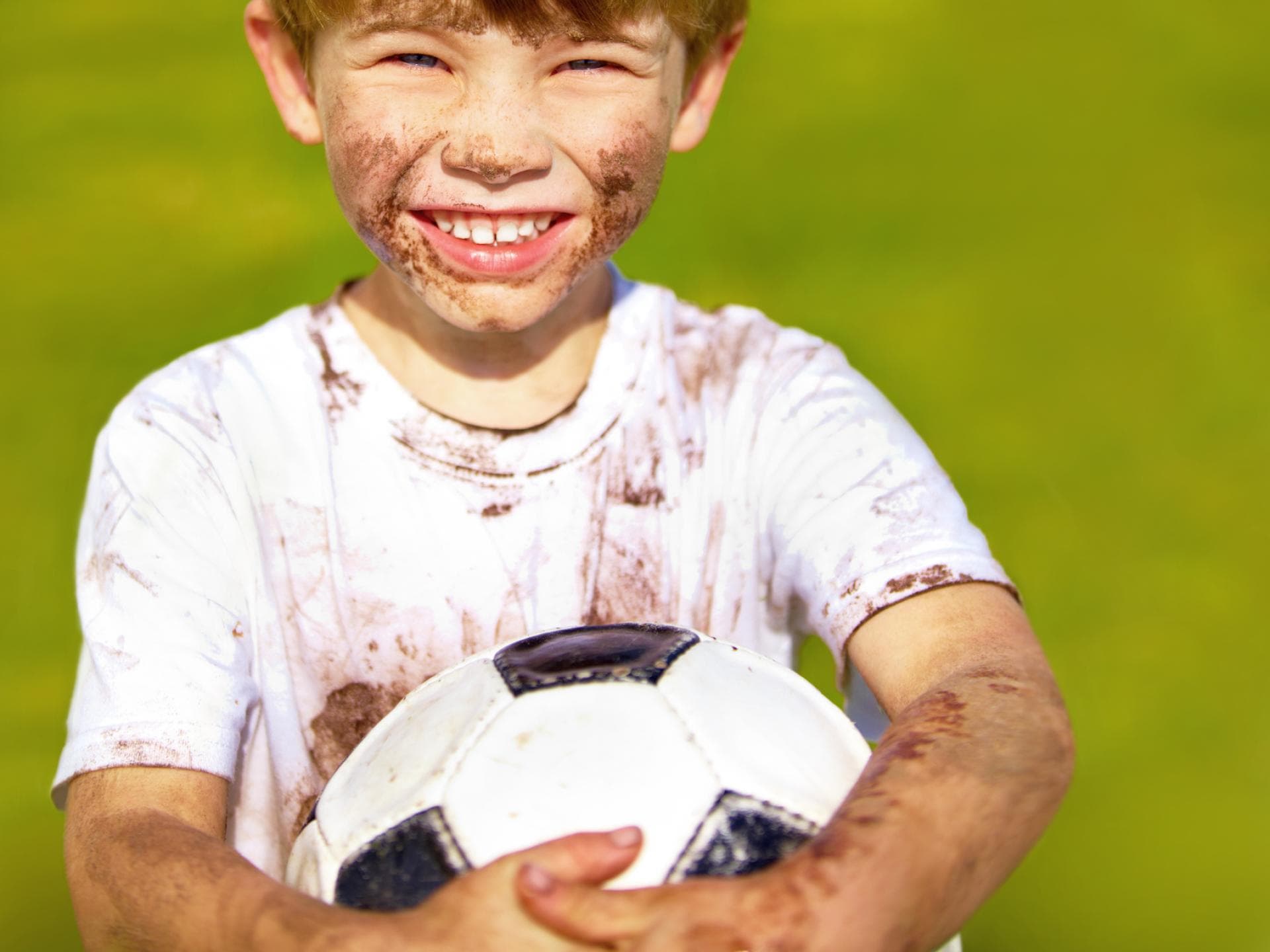 Verdrecktes fröhliches Kind mit Fußball.