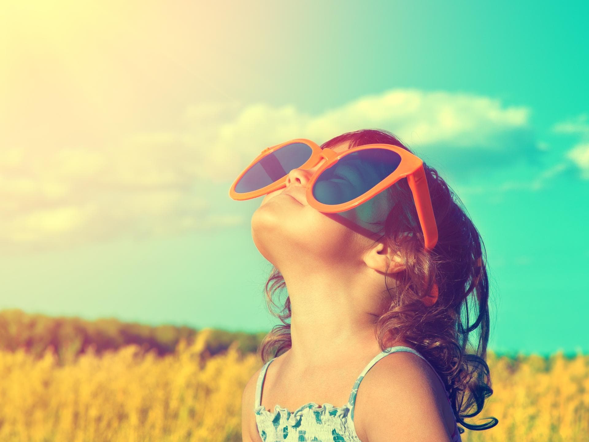 Kind schaut mit riesiger Sonnenbrille in den Himmel.