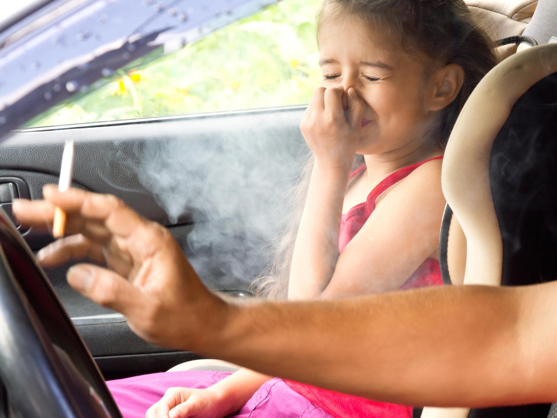 Kind hält sich wegen Zigarrettenrauch im Auto die Nase zu.