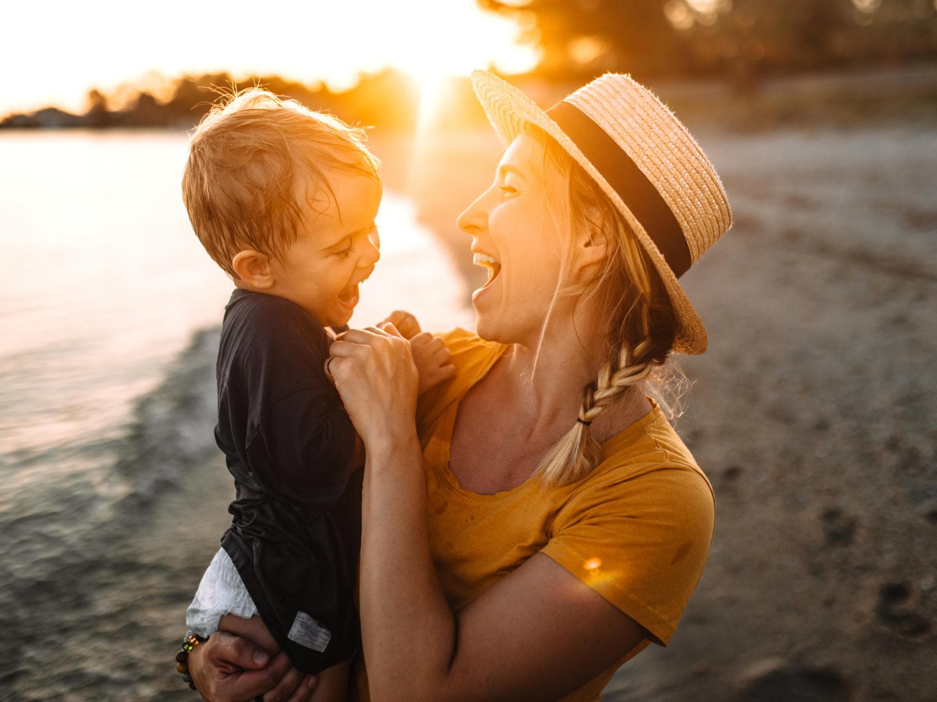 Das Leben mit Kind hält viele Lichtblick-Momente bereit. Mutter und Sohn lachend am Strand bei Sonnenuntergang.