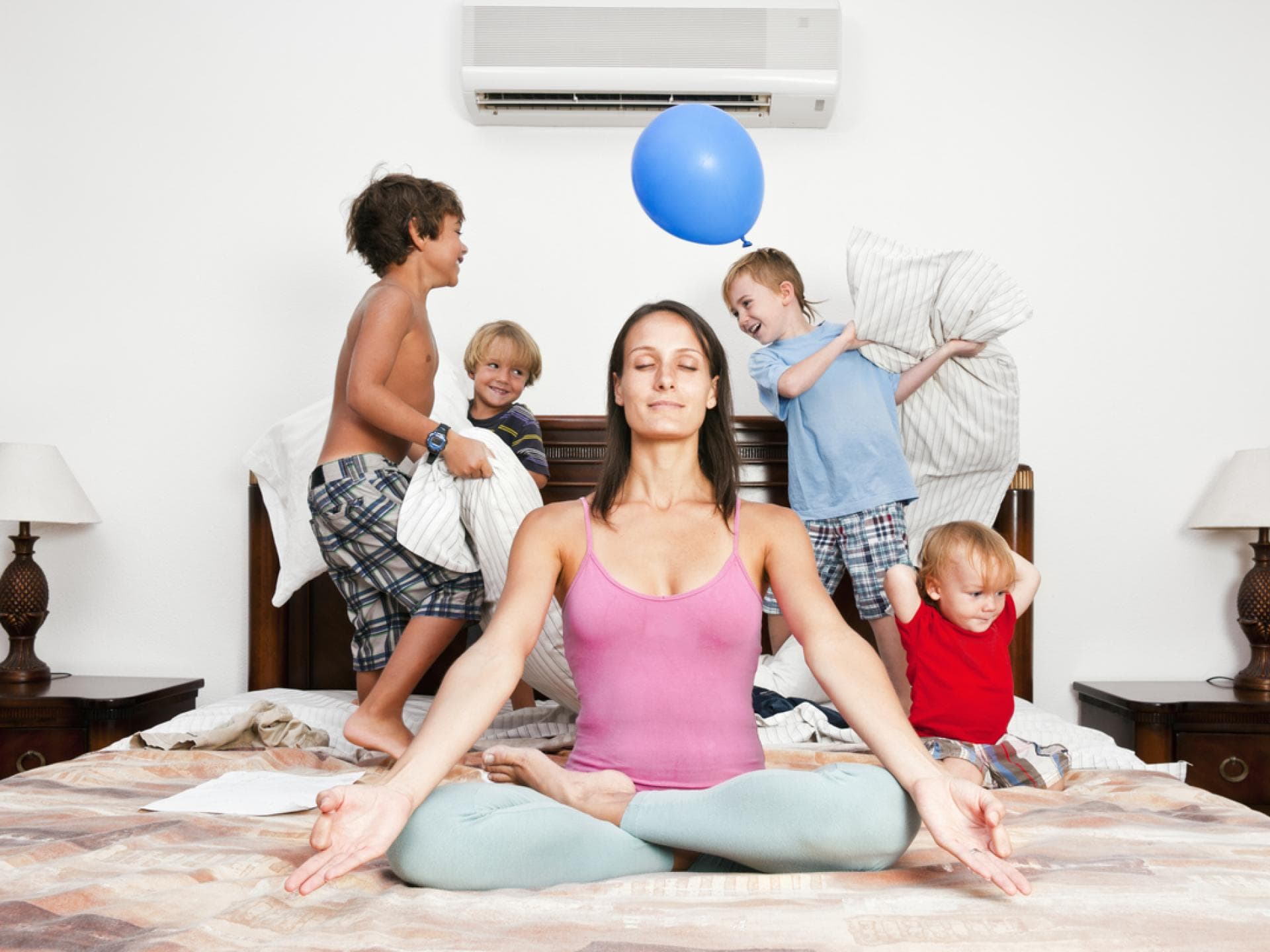 Es ist nicht einfach, im hektischen Alltag die Geduld zu bewahren. Mutter meditiert auf dem Bett, im Hintergrund toben die Kinder.