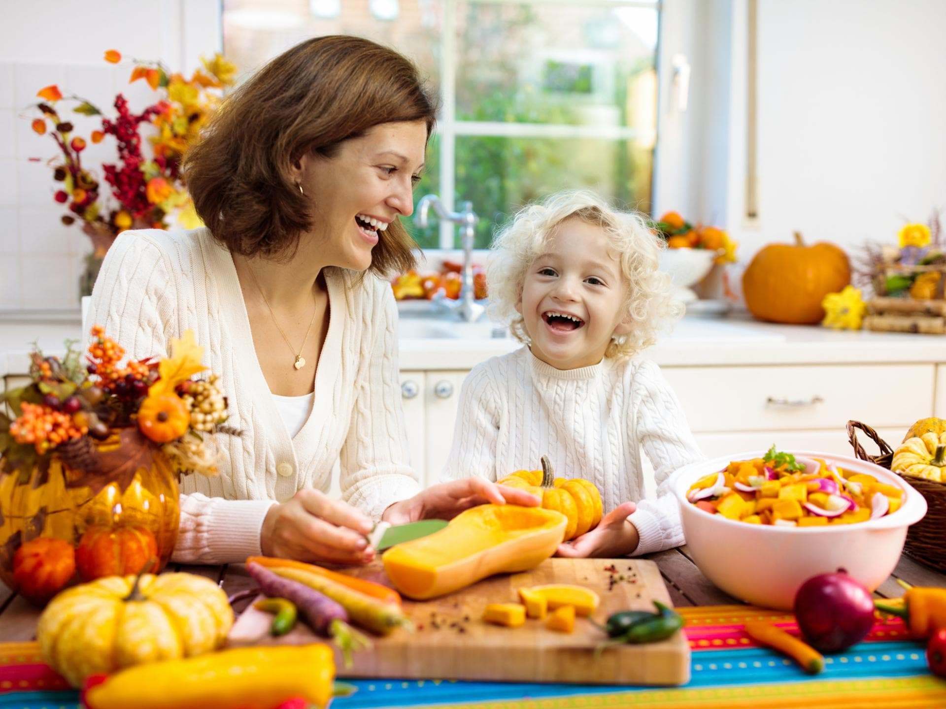 Mit Herbstgemüse lassen sich leckere und herzhafte Halloween-Rezepte zaubern. Fröhliche Mutter und Kind bereiten Kürbis zu.