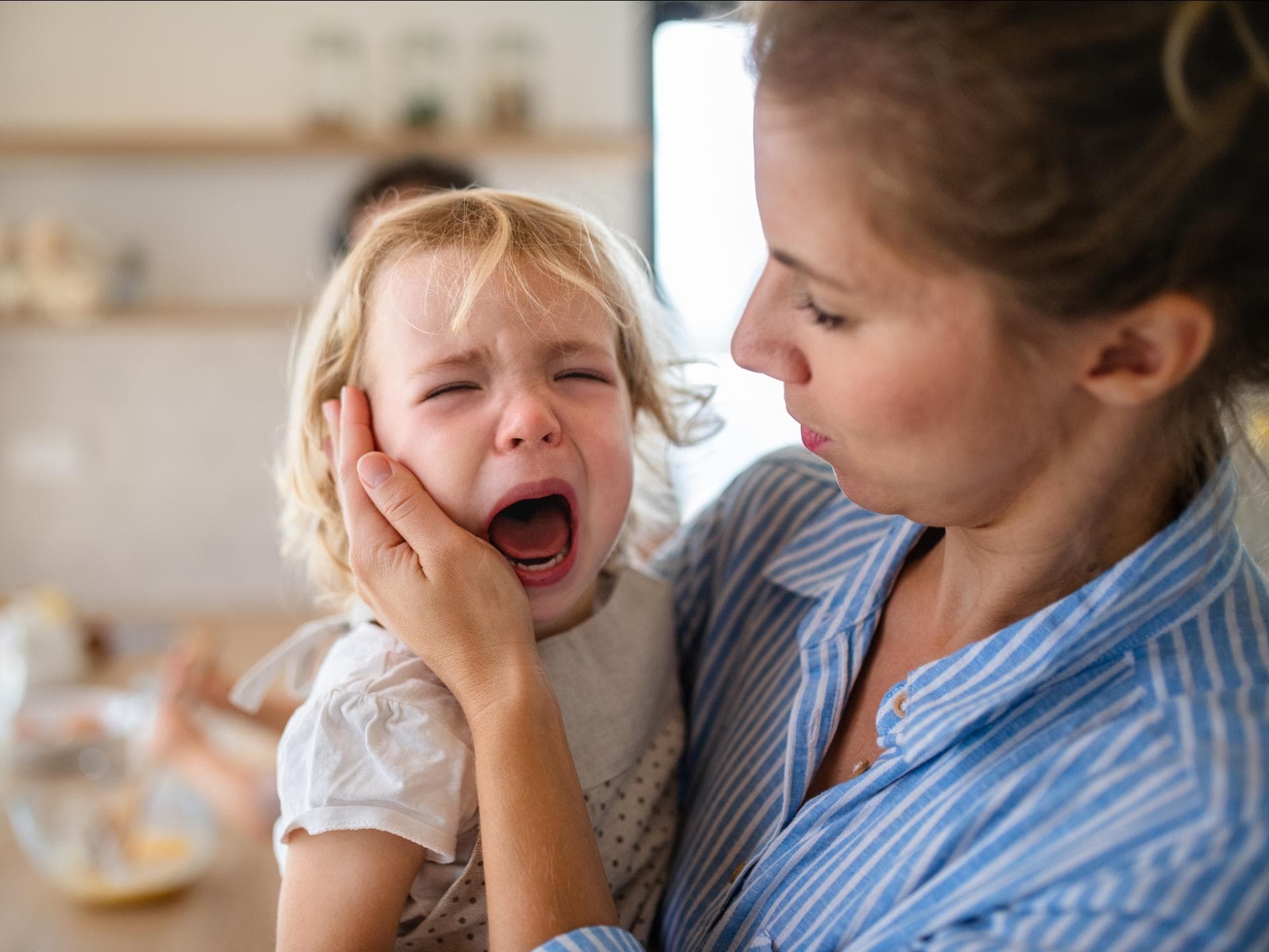Manchmal weinen Kinder nur, weil sie unsere Reaktion sehen. Mutter hält weinendes Kleinkind auf dem Arm.