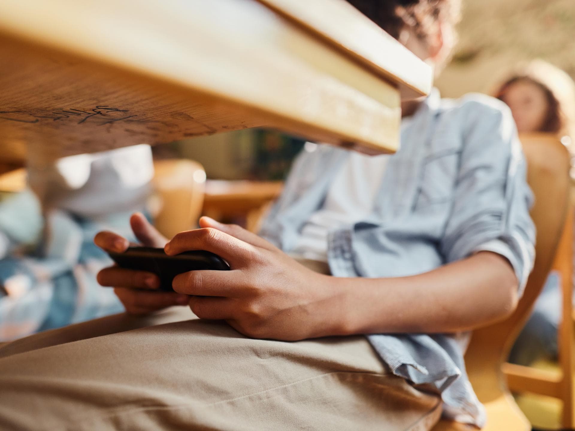 Ohne Smartphone in der Schule lernen Kinder besser. Junge spielt unter dem Schultisch am Smartphone.