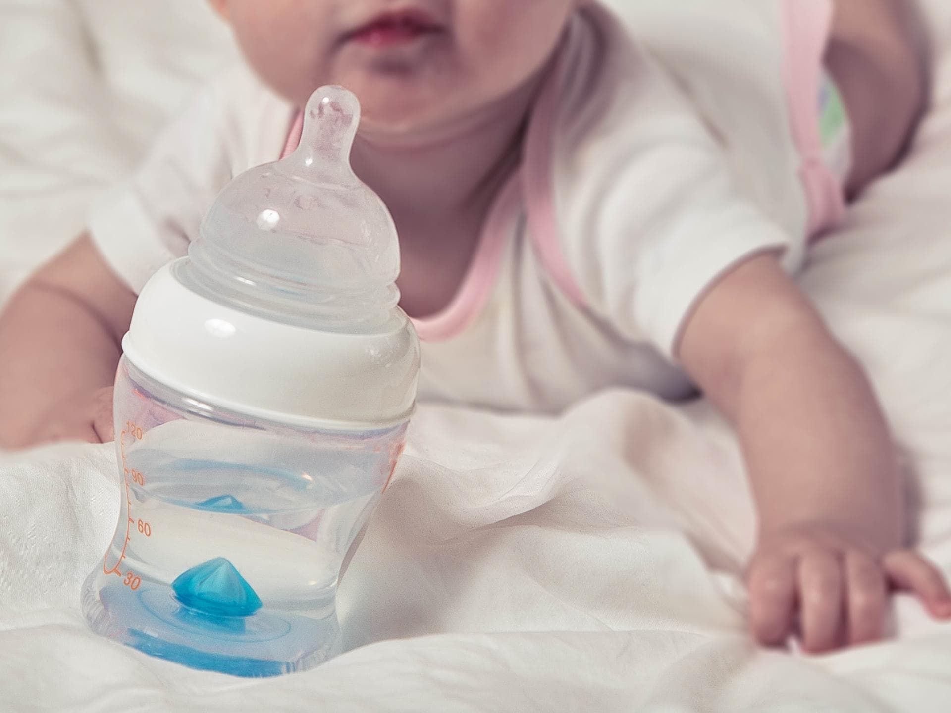 Baby mit Wasserflasche im Bett.