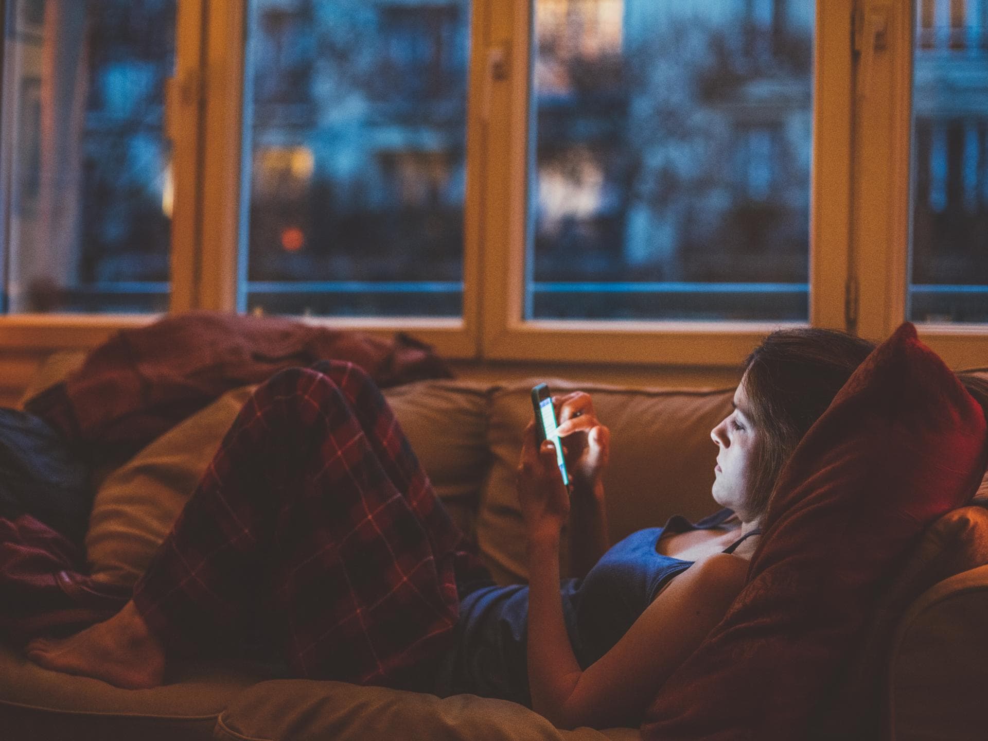 Fast alle Eltern lieben Foto-Rückblicke ihrer Kinder. Frau liegt auf dem Sofa und guckt auf ihr Handy.