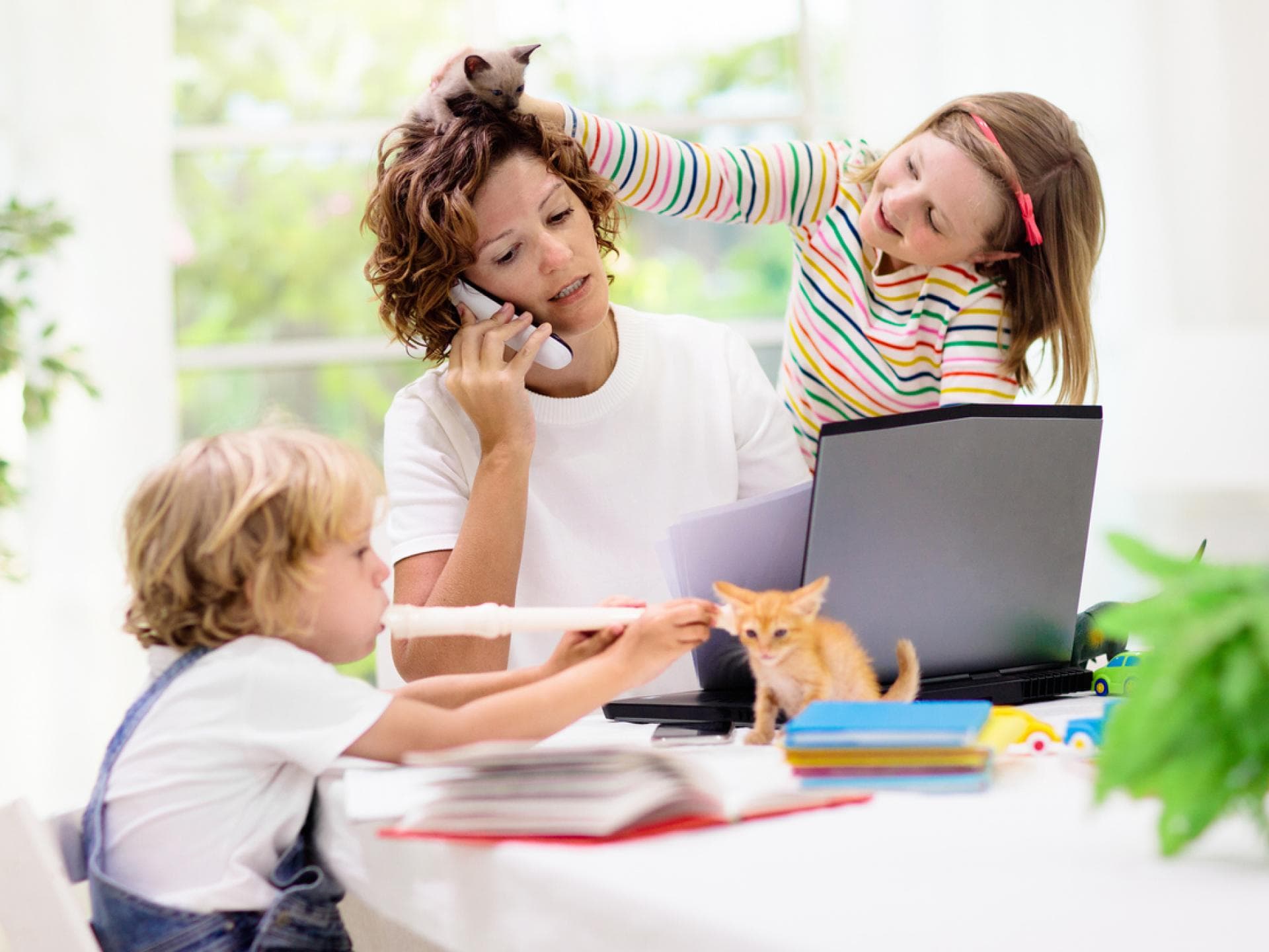 Mütter leiden oft unter der Mehrfachbelastung durch Job, Haushalt und Erziehung. Mutter am Laptop wird von zwei Kindern genervt.