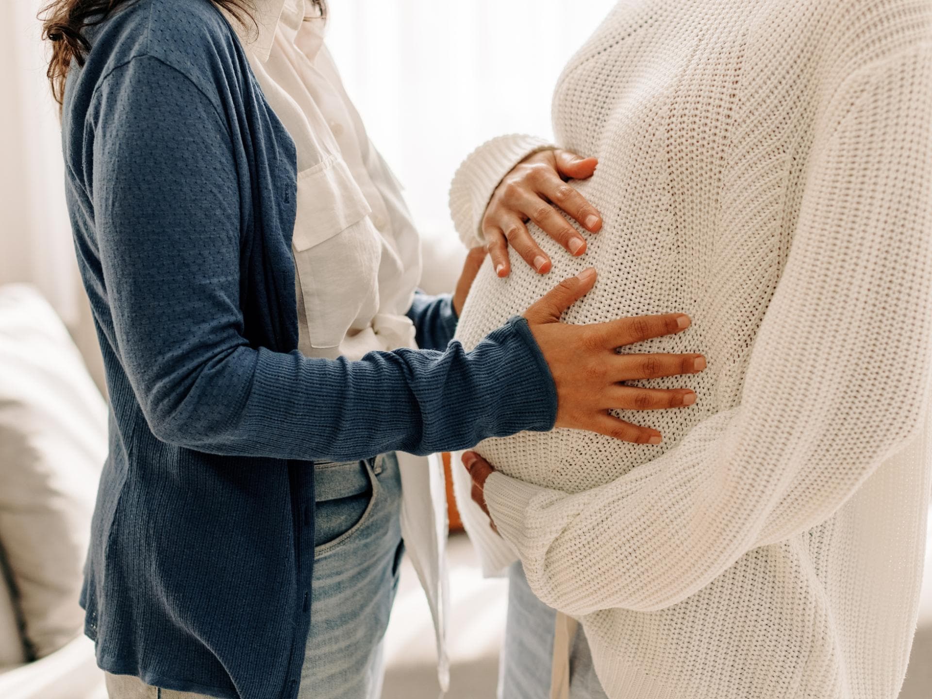 Eine Frau streichelt den schwangeren Bauch einer anderen Frau.
