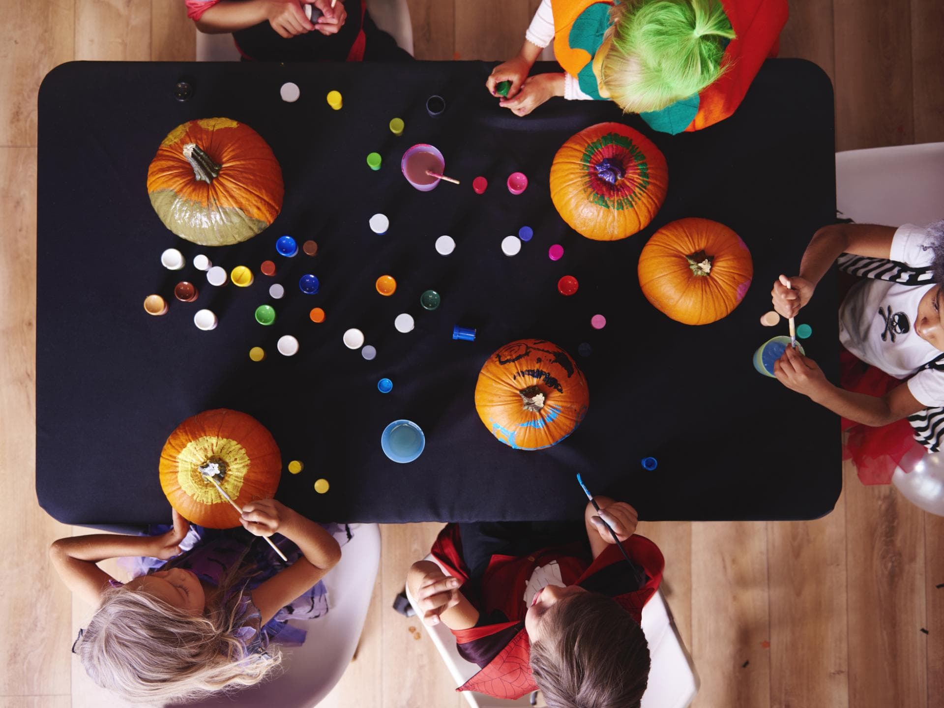 Kinder sitzen am Tisch und bemalen Kürbisse.