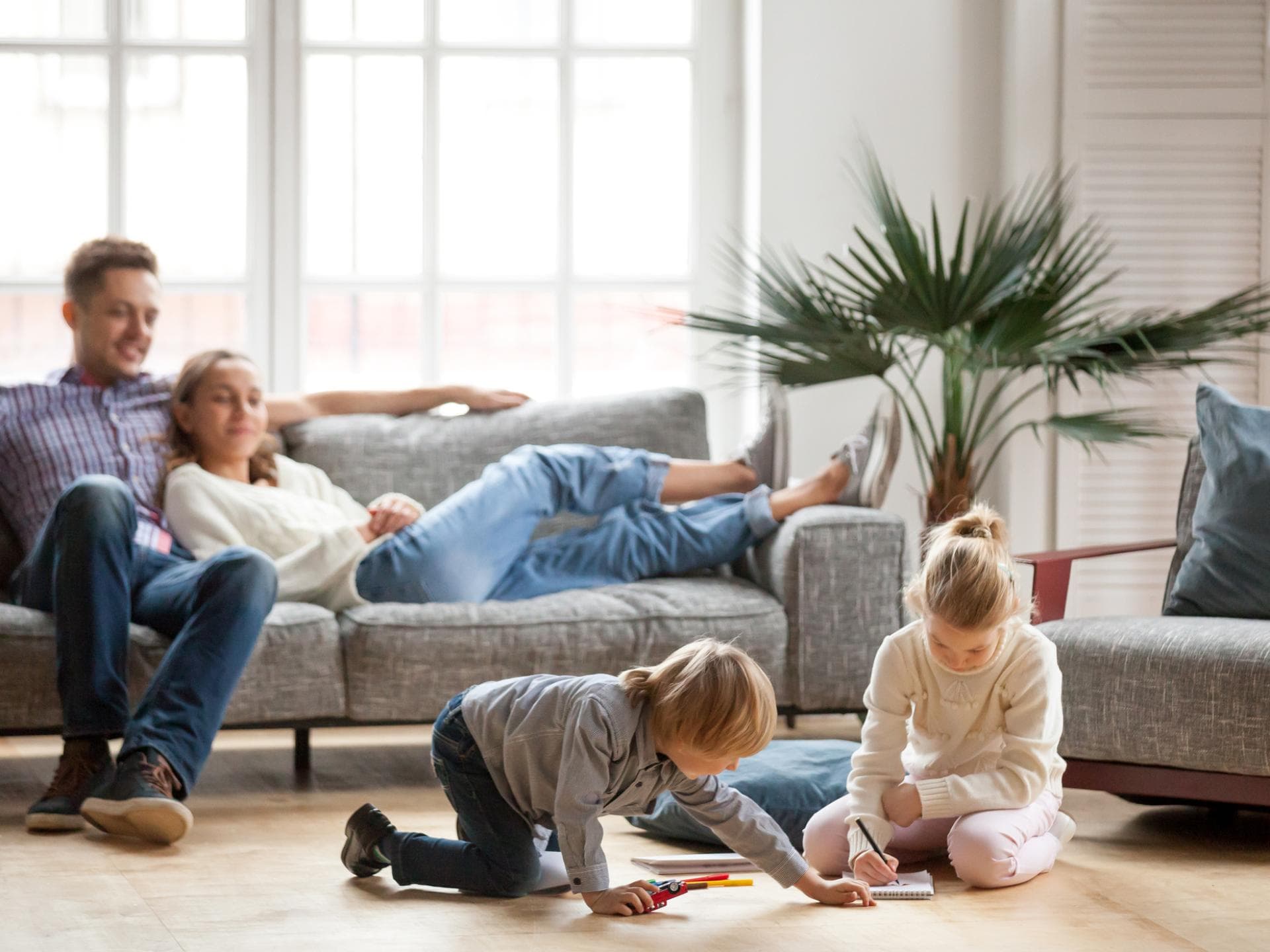 Beim Lazy Parenting geht es darum, Kinder Freiheiten zu gewähren. Eltern sitzen auf dem Sofa, Kinder spielen.