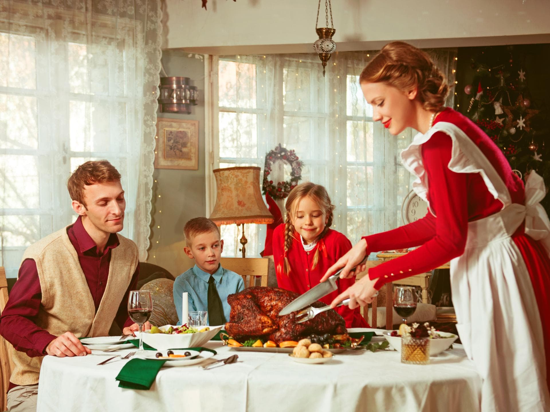 Tradwives machen sich hübsch und kümmern sich um häusliche Aufgaben. Frau im roten Kleid serviert ihrer Familie einen Braten.
