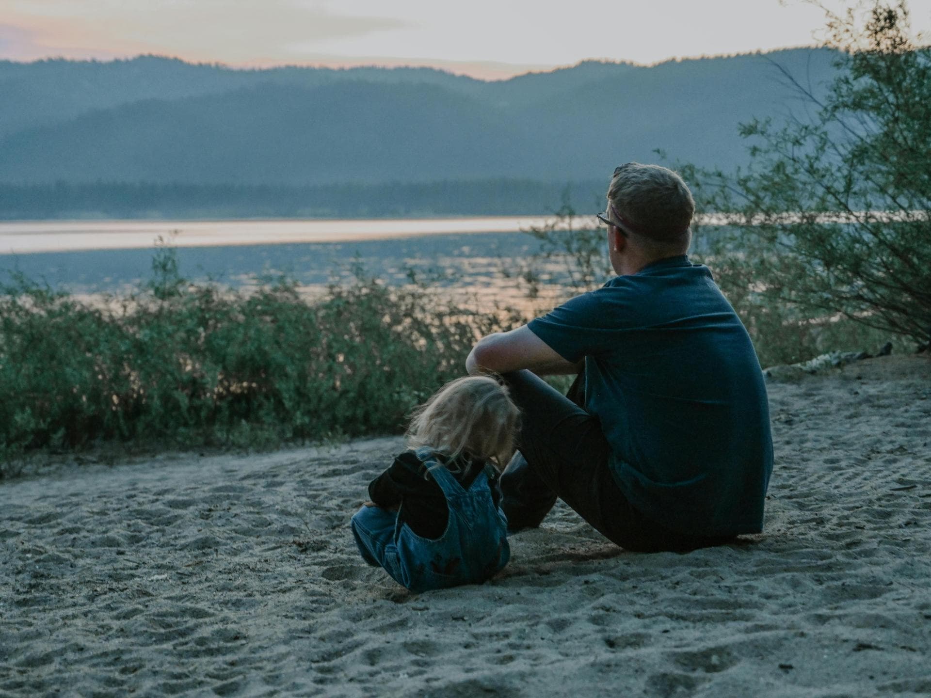 Der Urlaub ist nicht für alle Eltern entspannend. Vater sitzt mit Kleinkind am Strand.