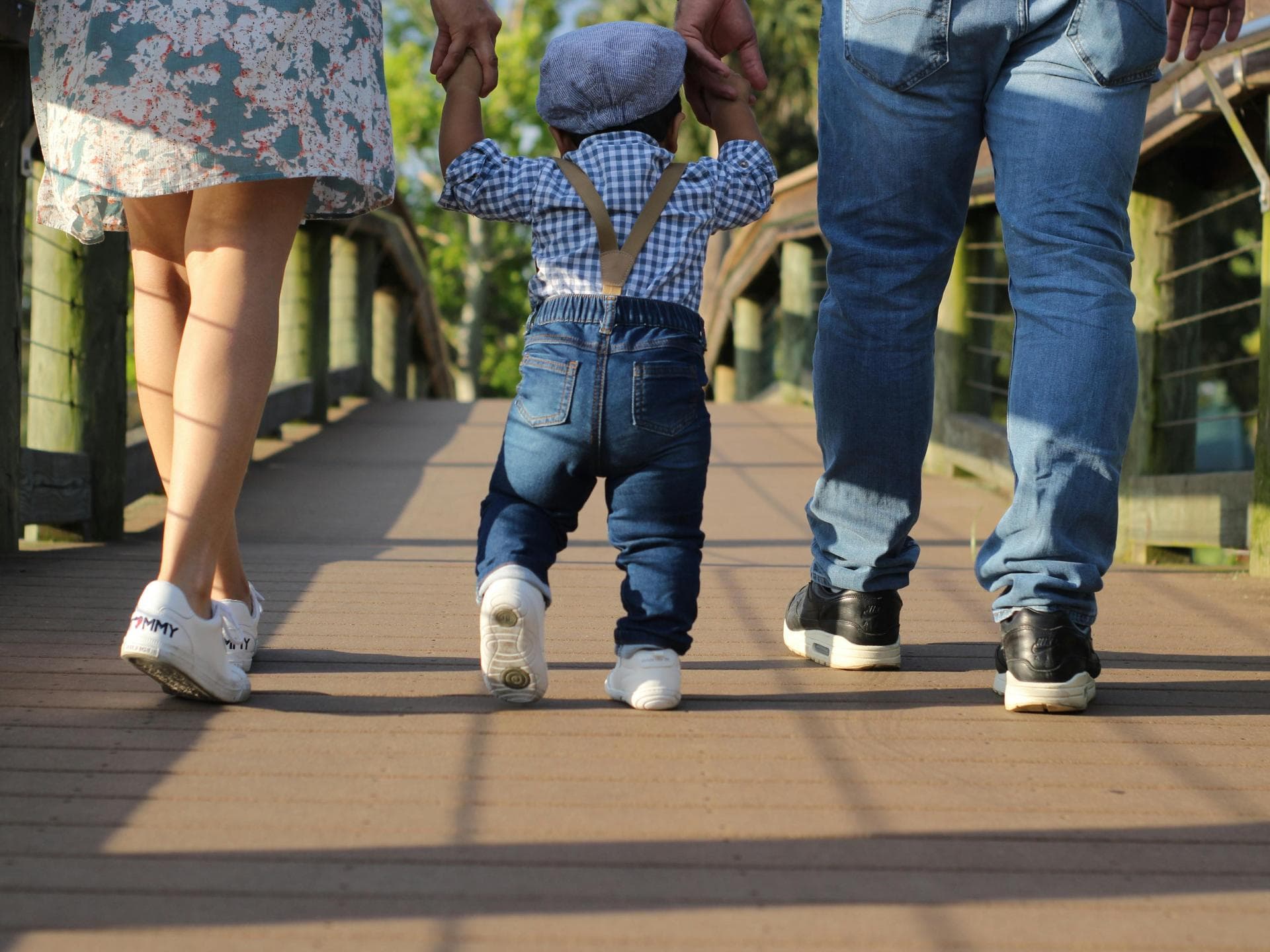 Lauflernschuhe elfen bei den ersten Schritten – aber wie lange können sie von Kindern getragen werden? Ein kleiner Junge macht läuft an der Hand seiner Eltern.
