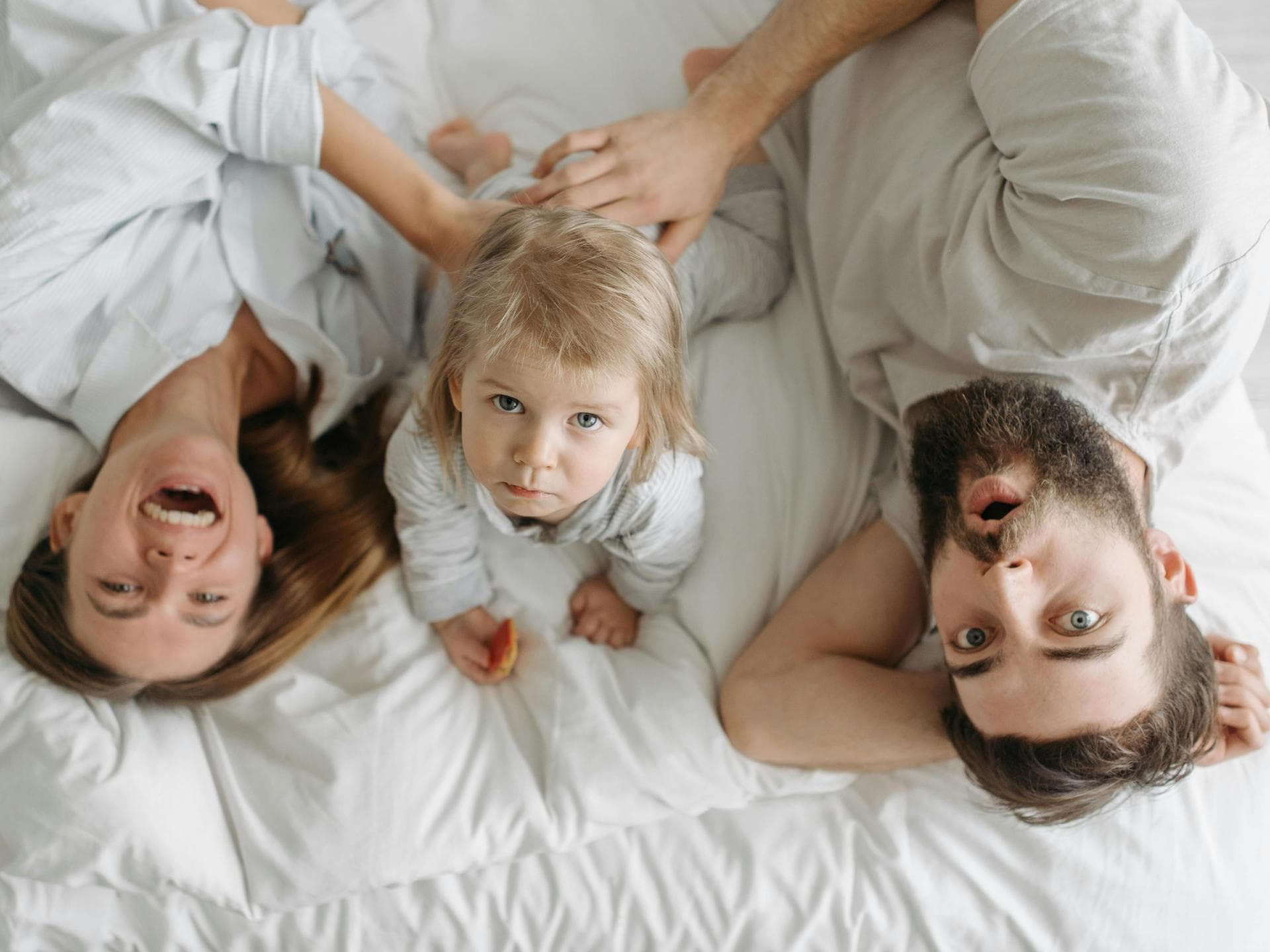 Eltern liegen mit Baby auf dem Bett und machen Quatsch.