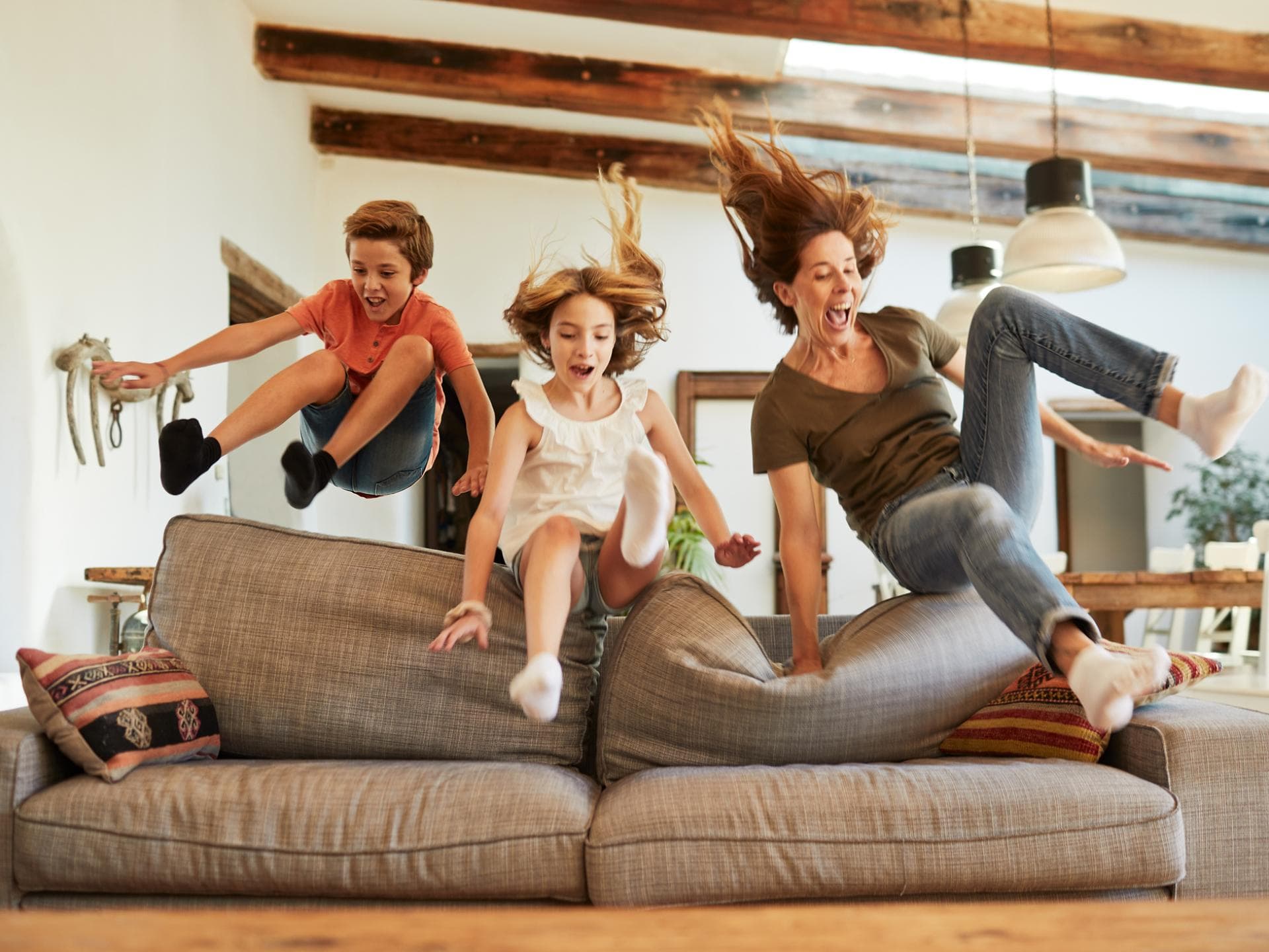 Mutter und zwei Kinder springen zusammen aufs Sofa