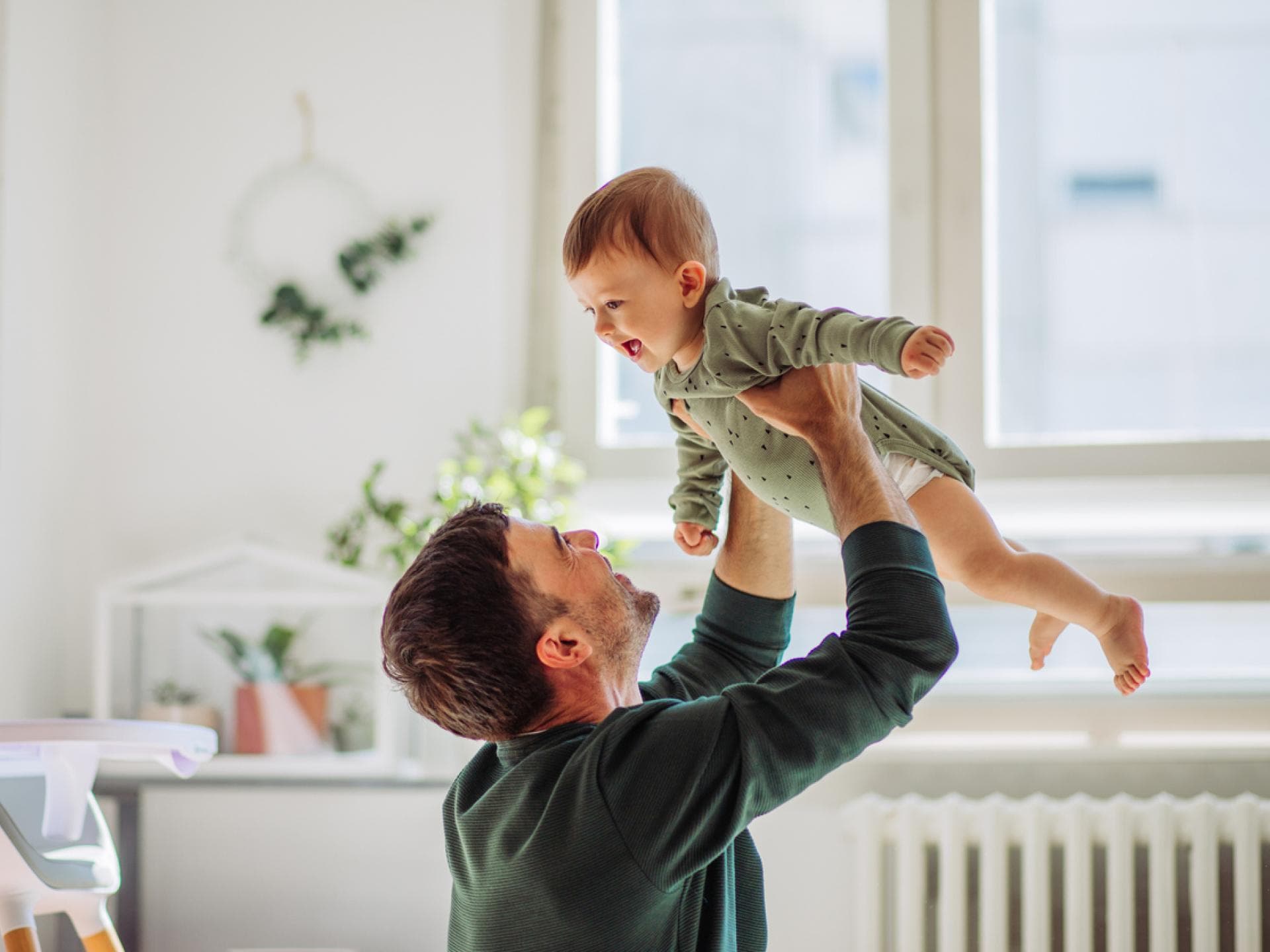 Die Erziehung wirkt sich auf die Gehirnentwicklung von Kindern aus. Papa hebt lachendes Baby in die Luft.