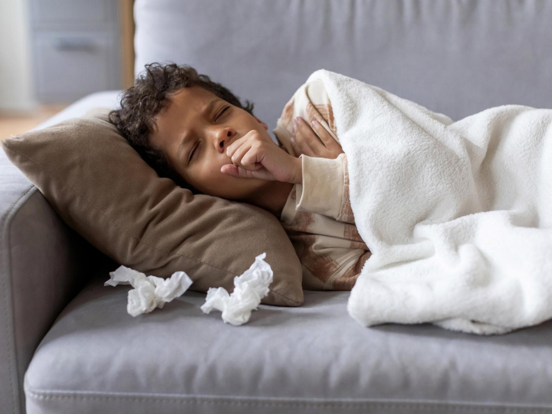 Die Keuchhusten-Zahlen bei Kindern und Jugendlichen sind stark gestiegen. Krankes Kind liegt auf dem Sofa.