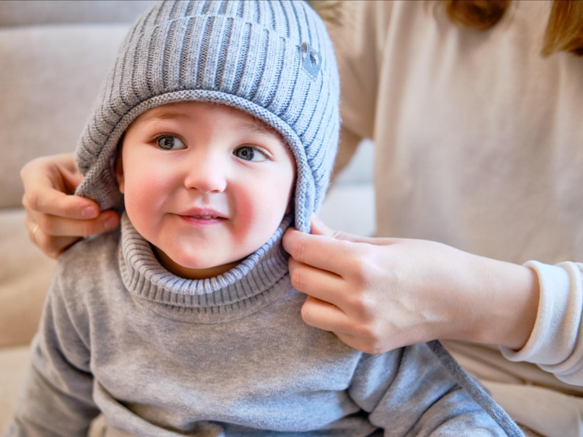 Kleinkind bekommt von der Mutter eine Mütze aufgesetzt.