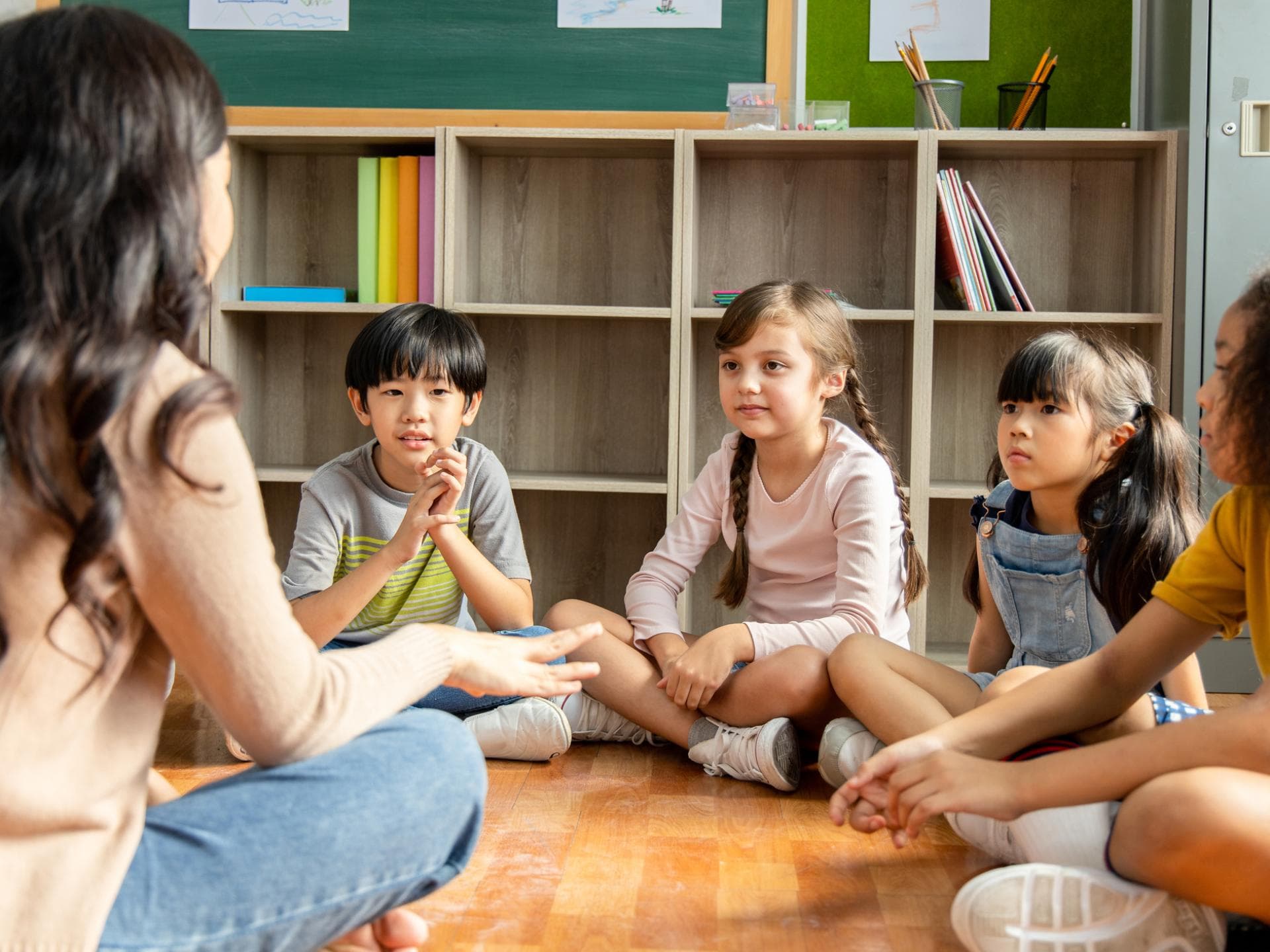 Grundschullehrerin erklärt wichtige Regel. Lehrerin sitzt mit Grundschulkindern auf dem Boden.