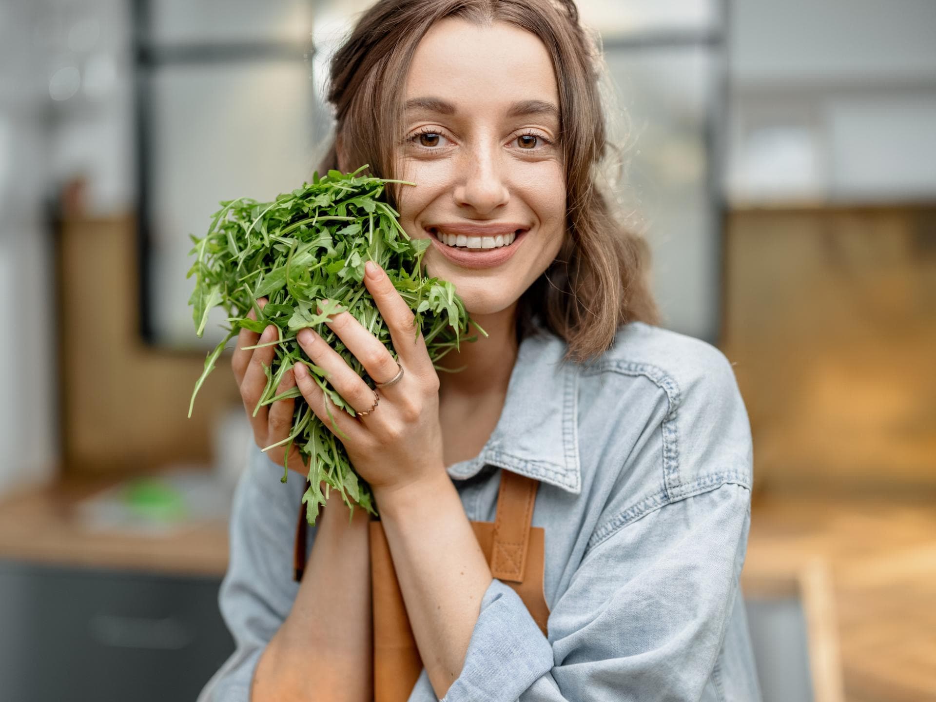 Viele schätzen den leicht bitteren Geschmack von Rucola. Fröhliche Frau halt einen Büschel Rucola in den Händen.