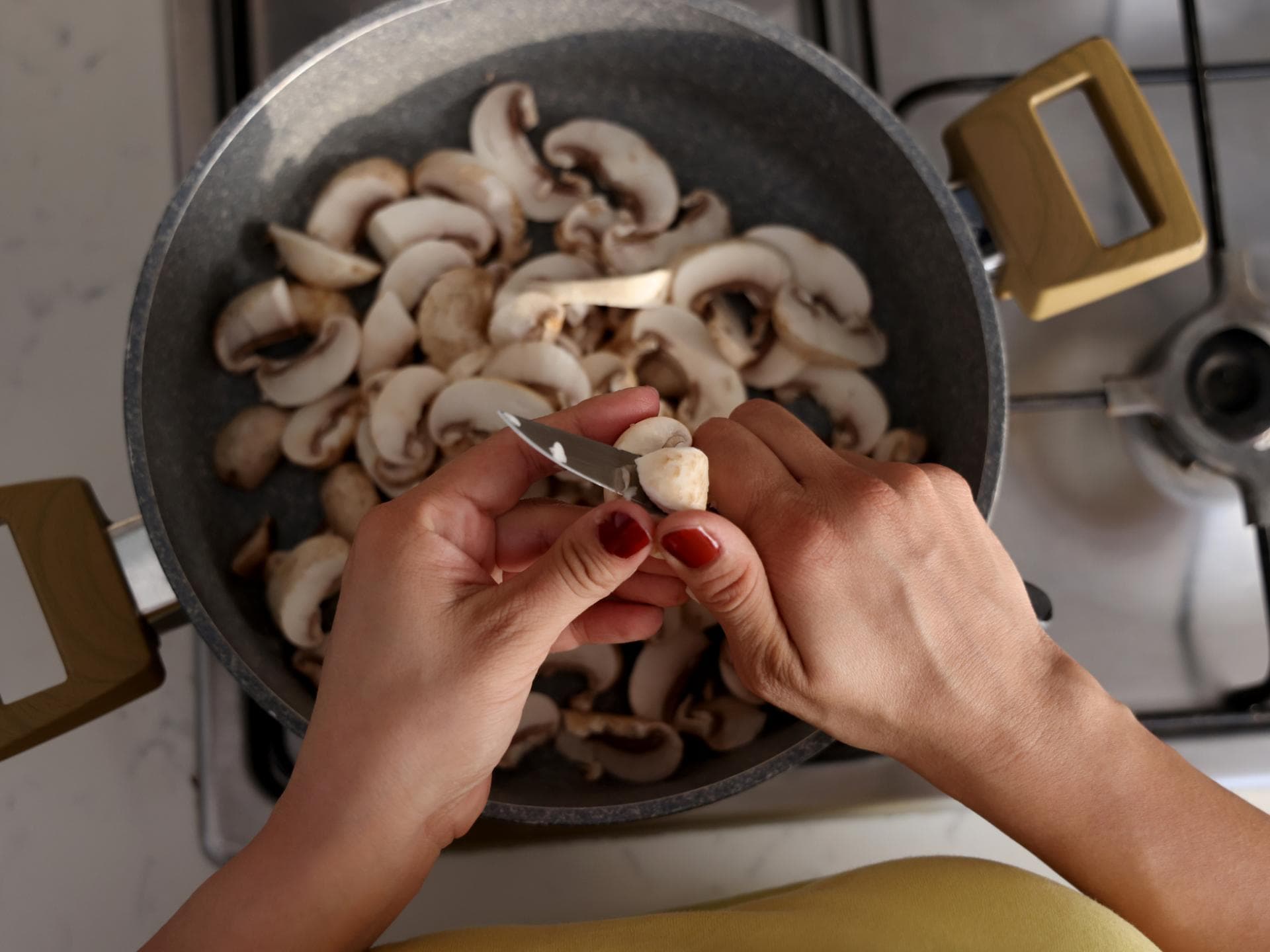 Frau schneidet Champignons in eine Pfanne.