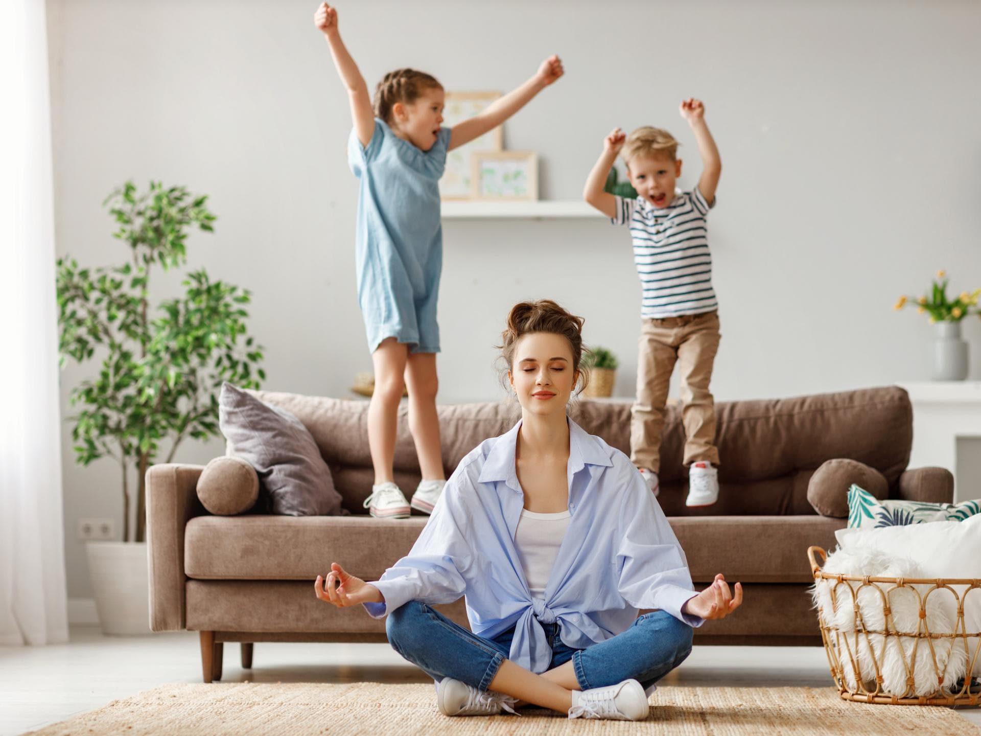 Kinder springen auf dem Sofa, Mutter meditiert.