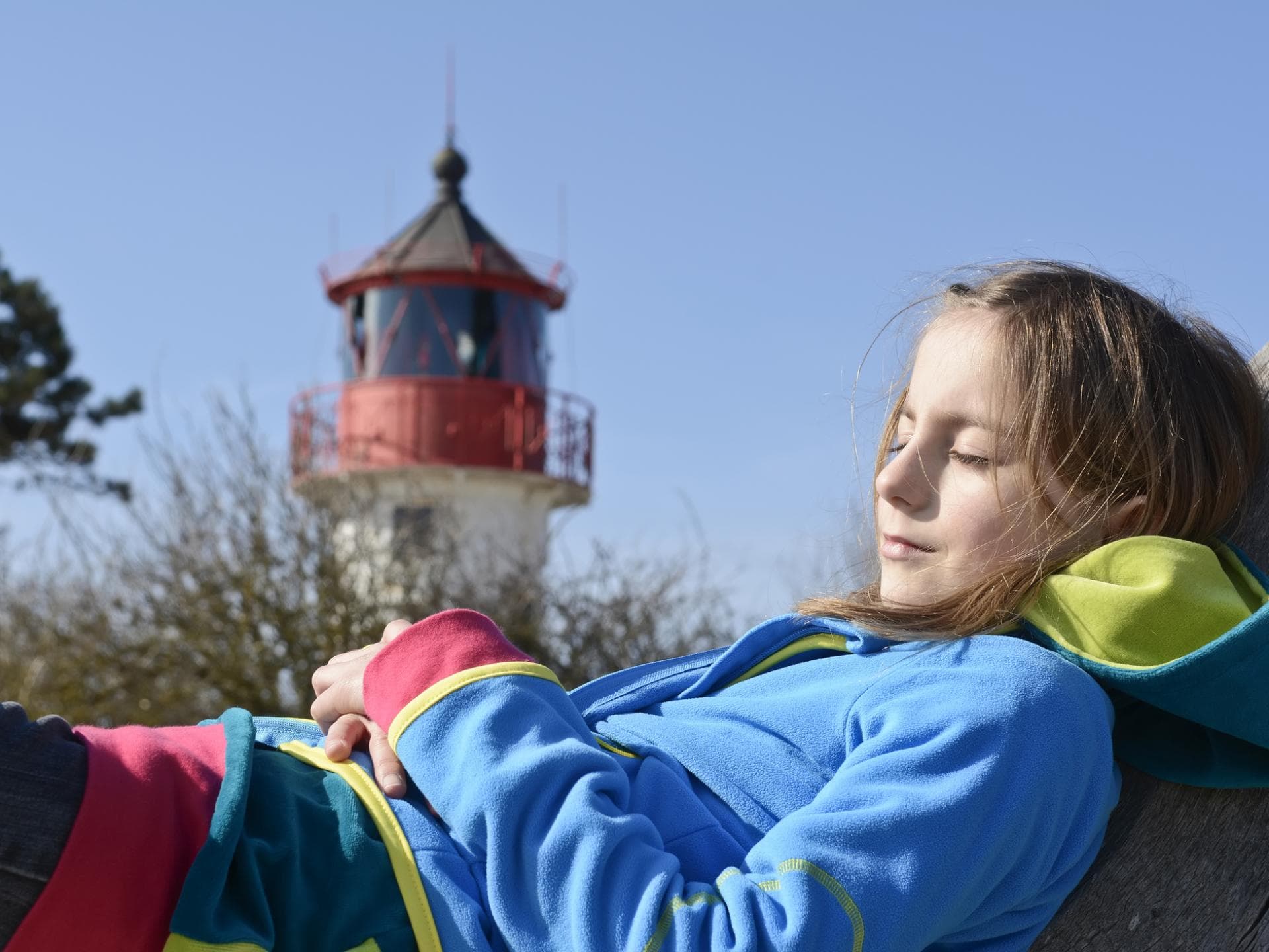 Leuchtturm-Eltern geben Halt. Mädchen chillt vor einem Leuchtturm.