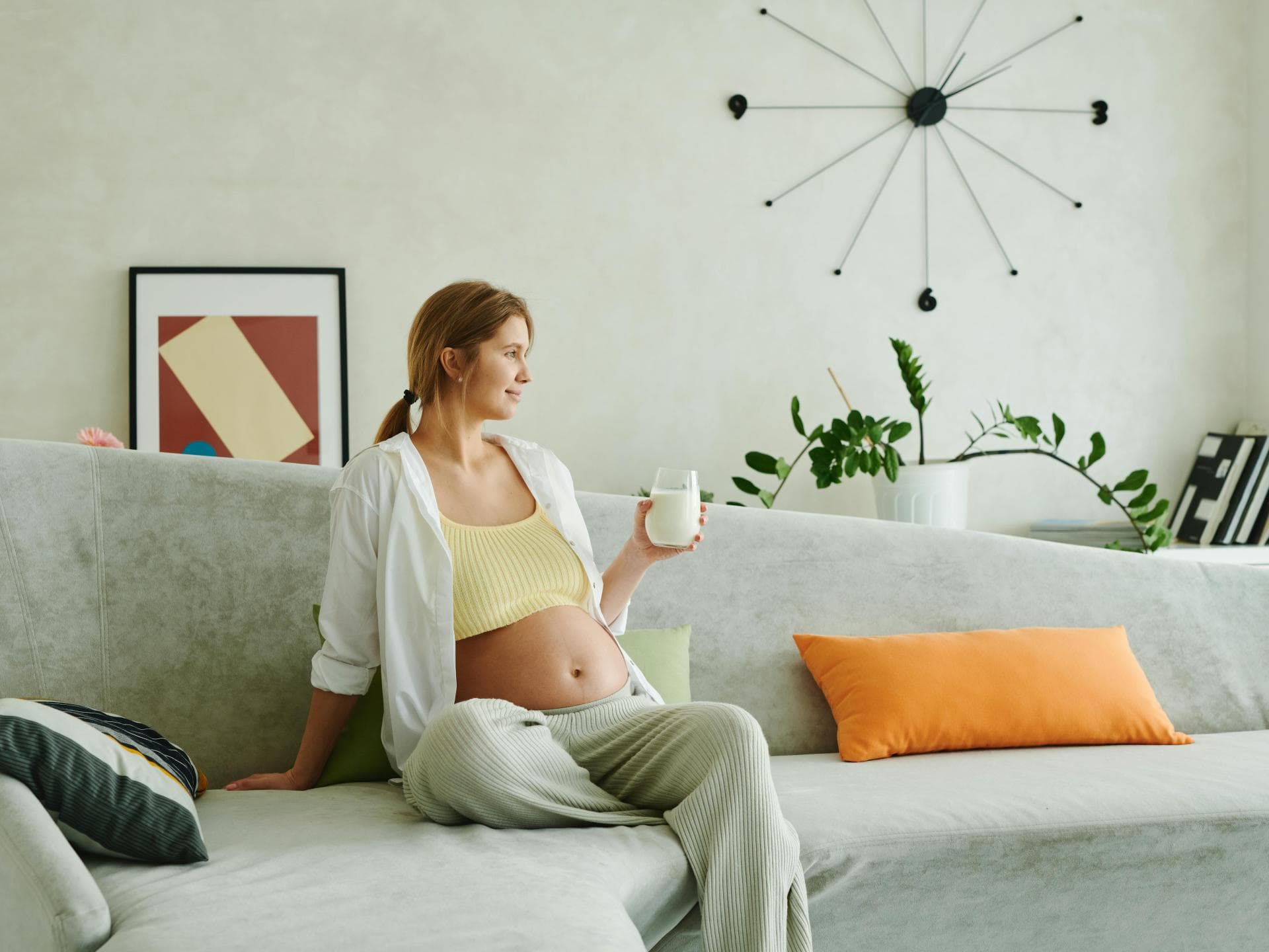 Schwangere Frau trinkt Buttermilch auf dem Sofa.