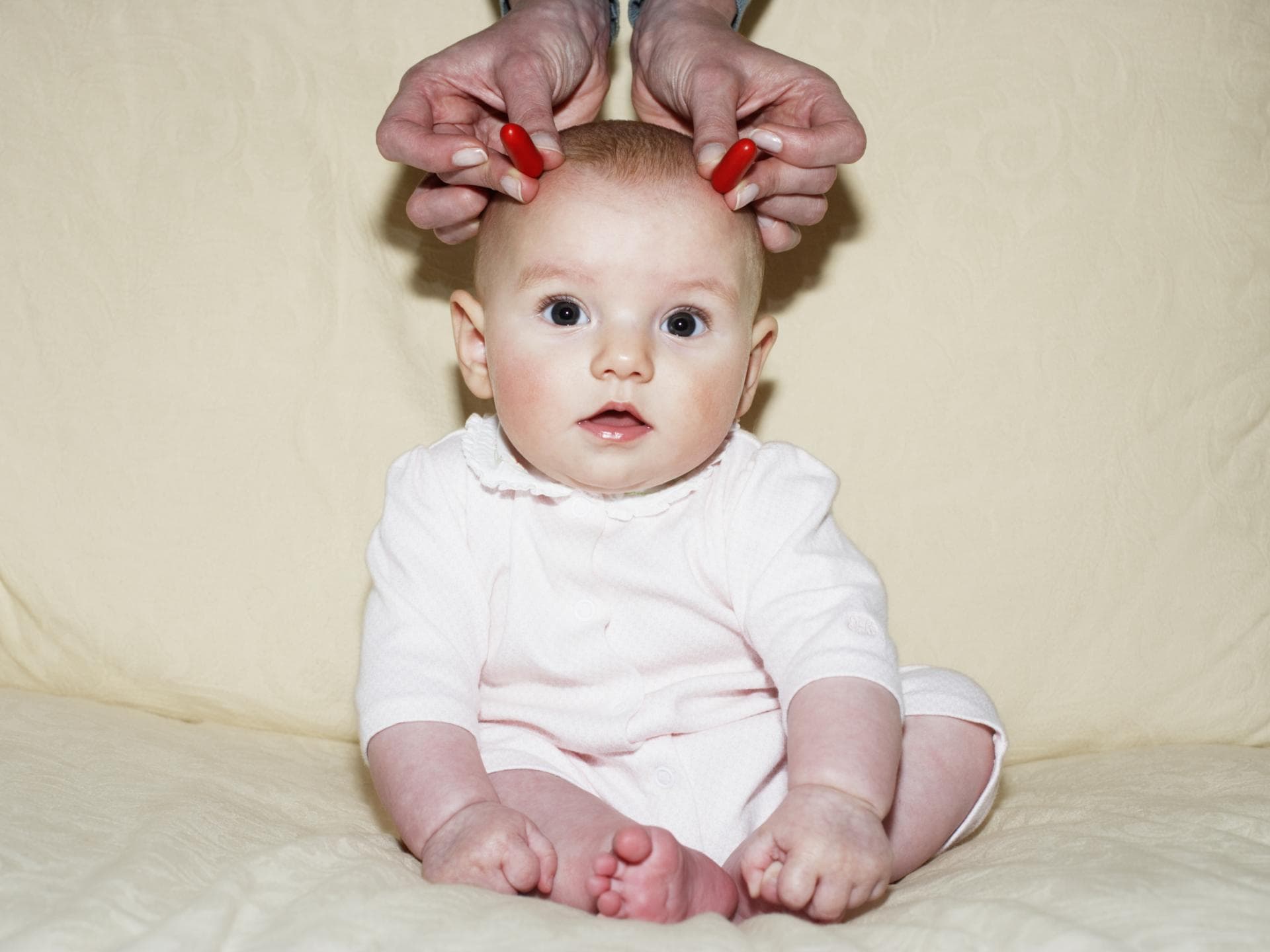 Baby bekommt rote Hörner an die Stirn gehalten.
