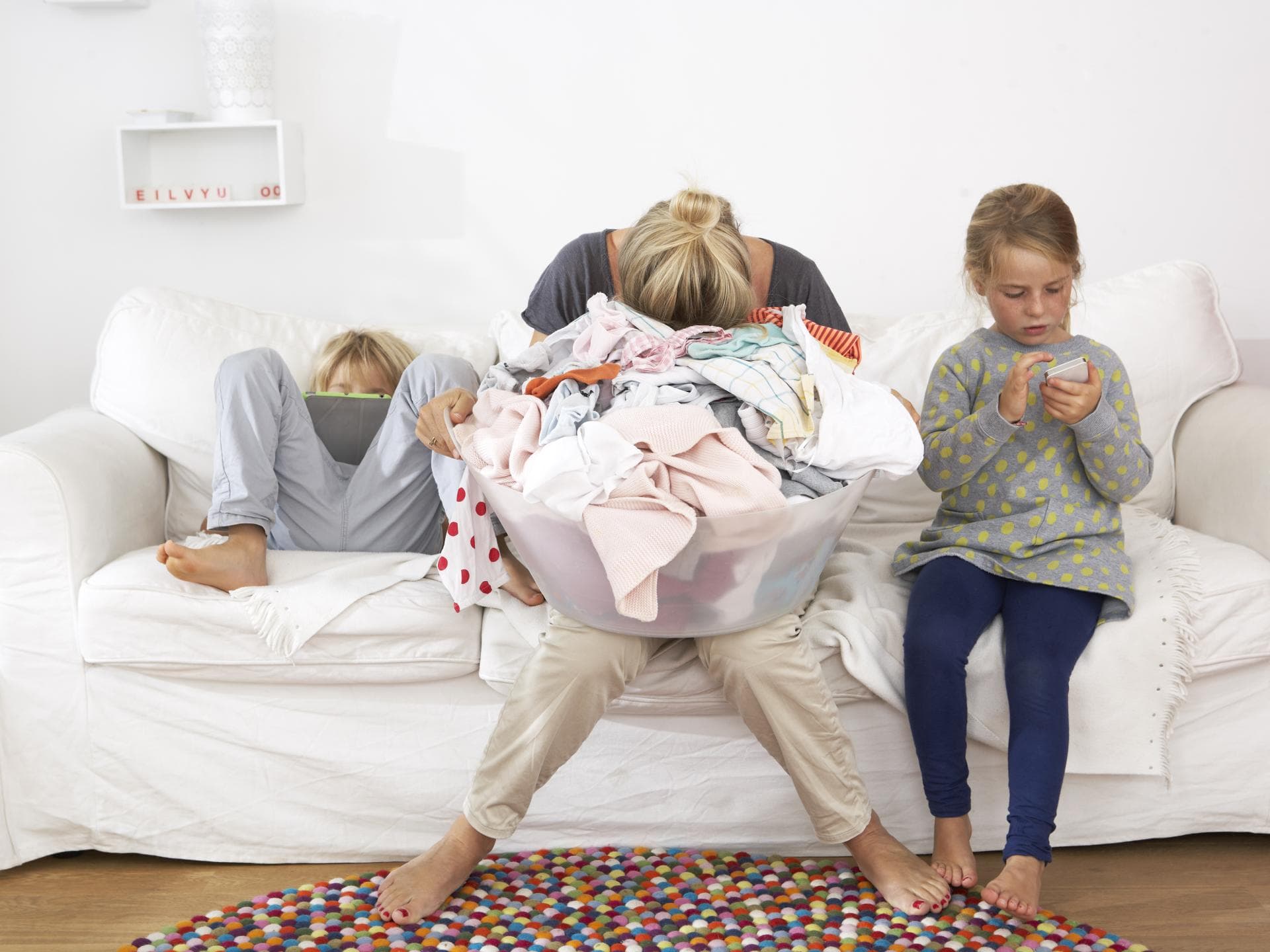 Viele Eltern fühlen sich im Alltag überfordert. Erschöpfte Mutter Wäschekorb auf dem Schoß auf dem Sofa.