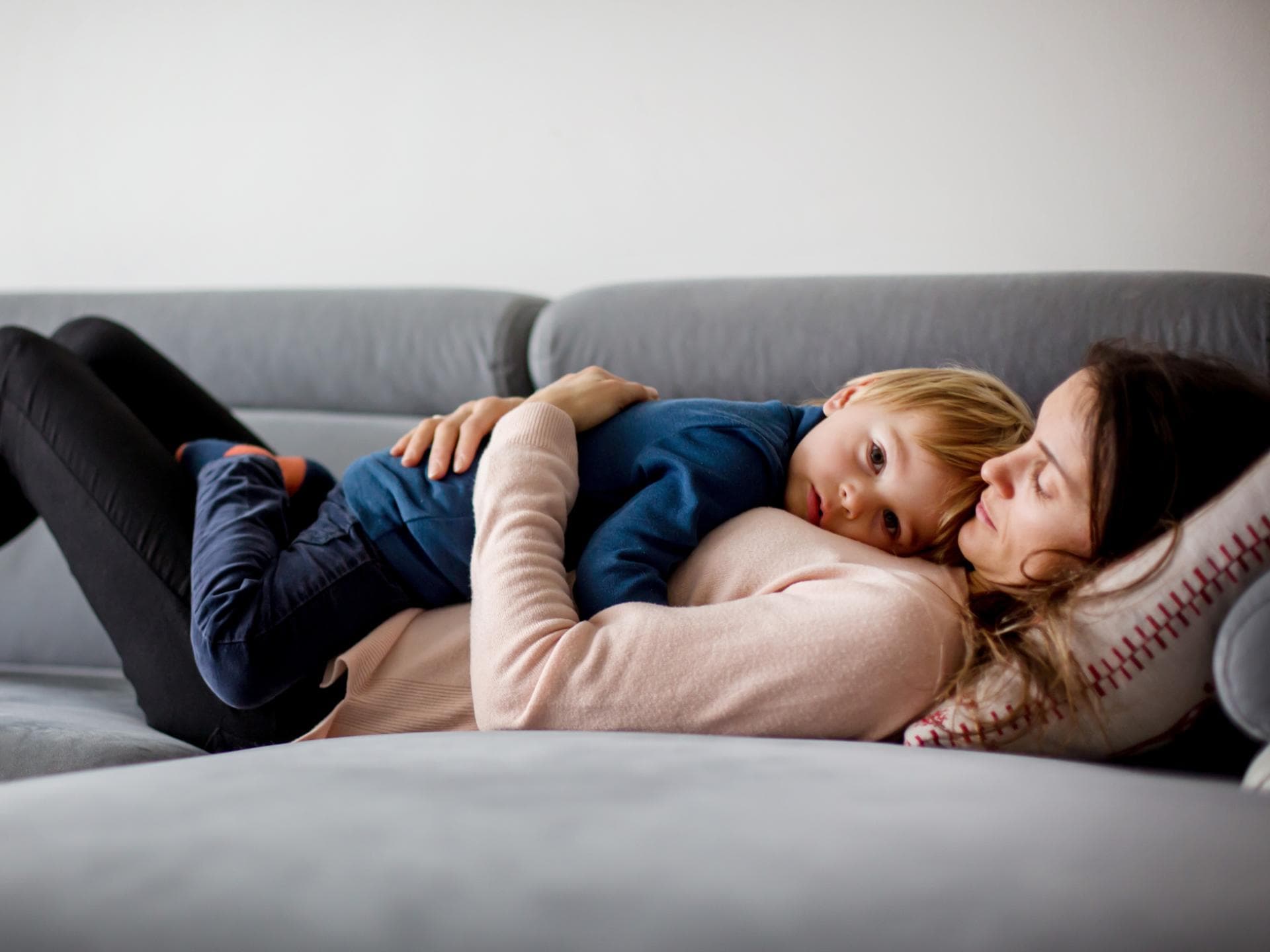 Wenn Kinder krank sind, wirkt Kuscheln Wunder. Mutter hält krankes Kind, liegen zusammen auf einer Couch.