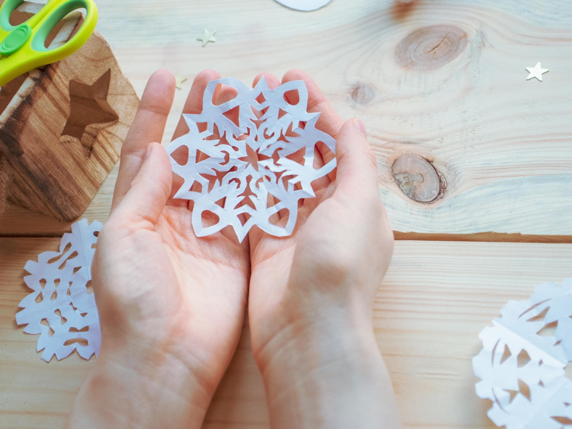 Kind hält selbst gebastelte Schneeflocke in der Hand.