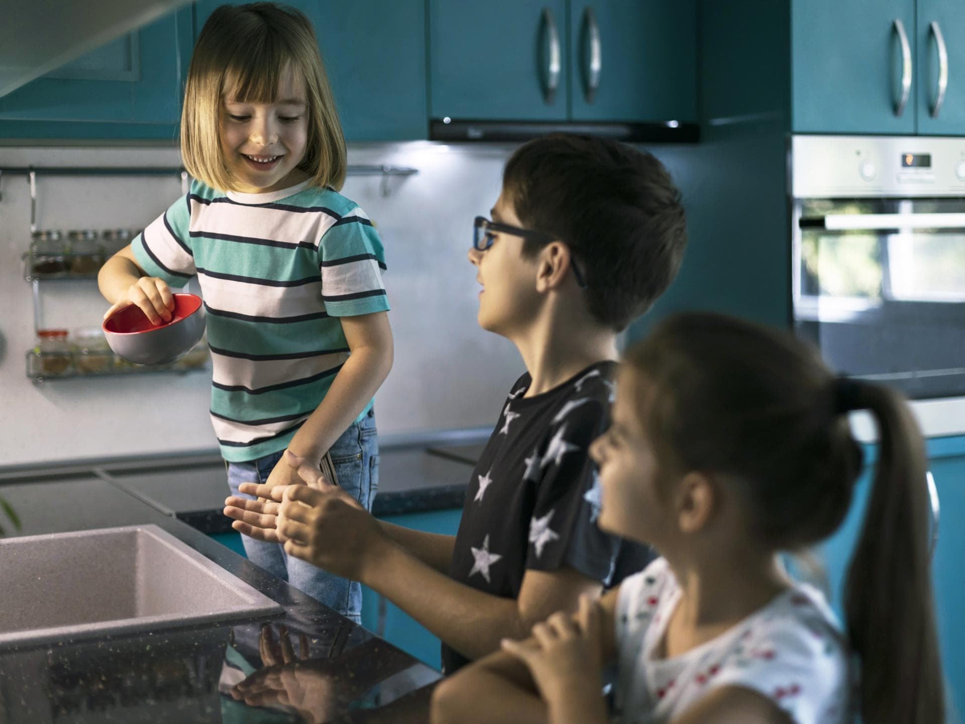 Gemeinsam machen Aufgaben mehr Spaß. Drei Kinder am Spülbecken.