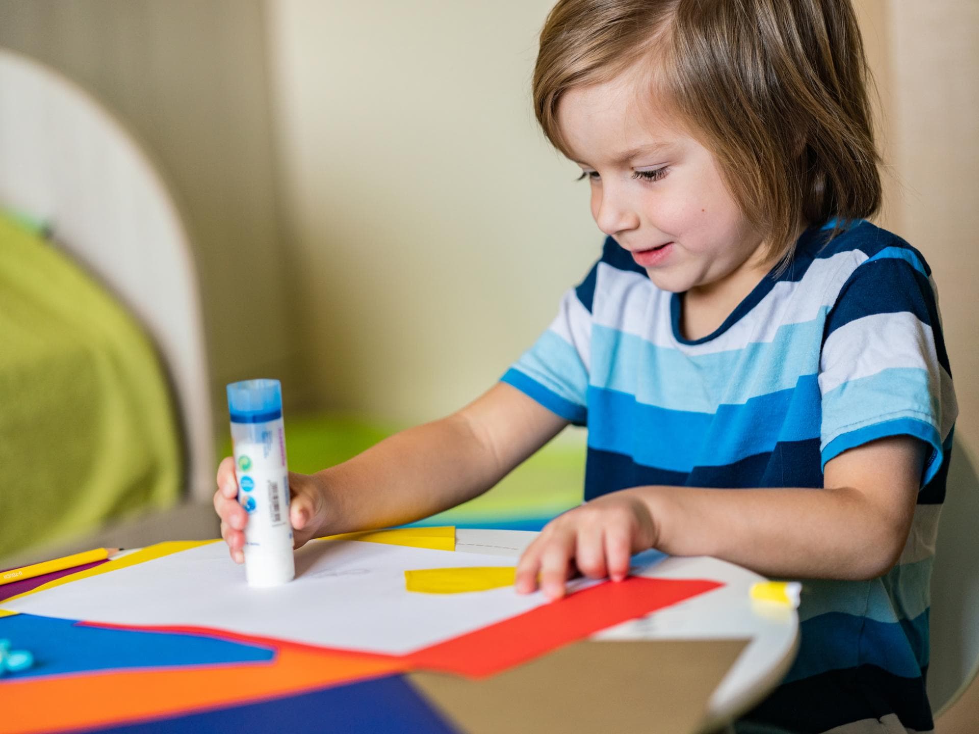 Kind mit Klebestift und buntem Papier.
