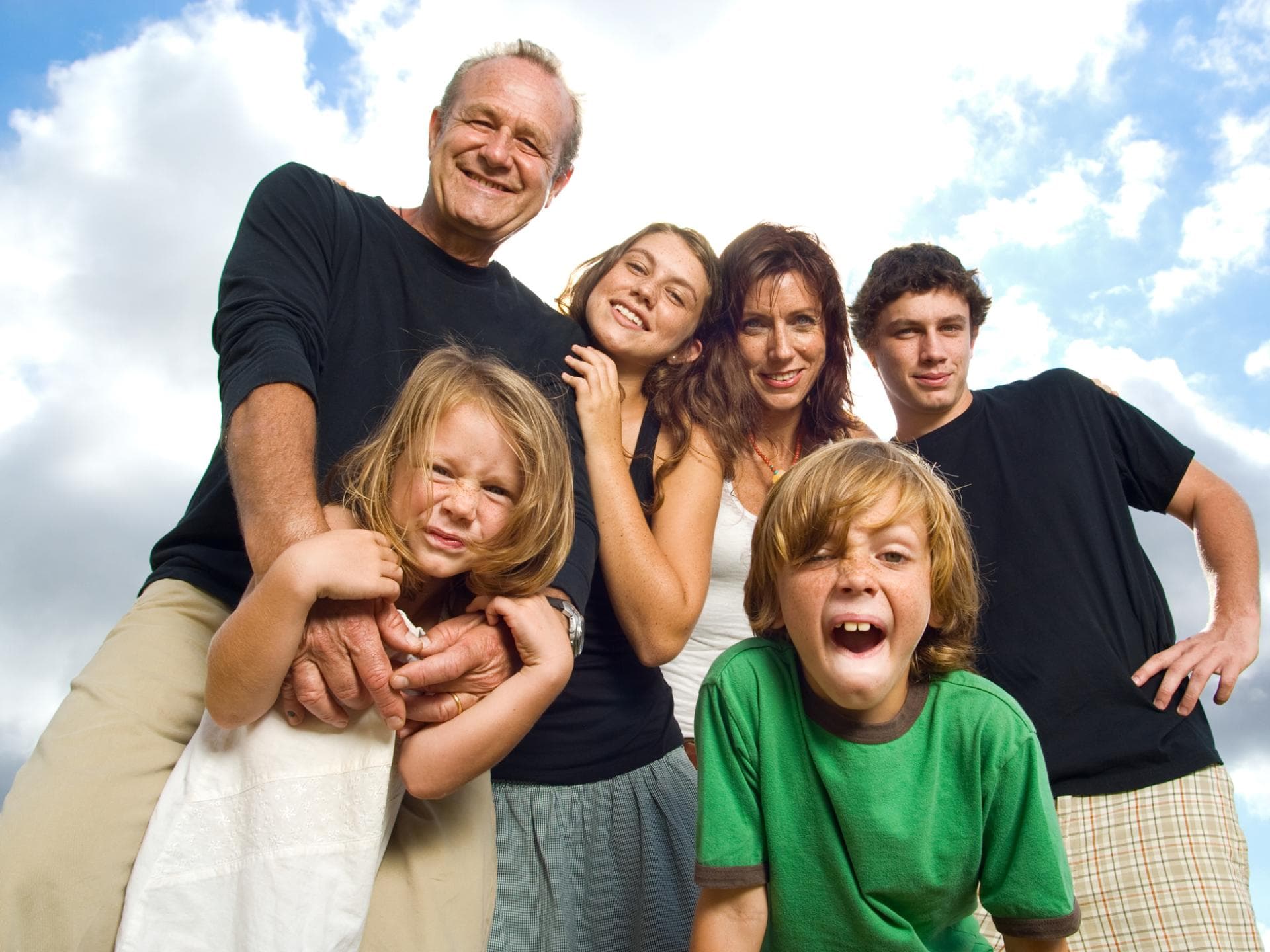 Patchworkfamilie mit vier Kindern vor blau-wolkigem Himmel.